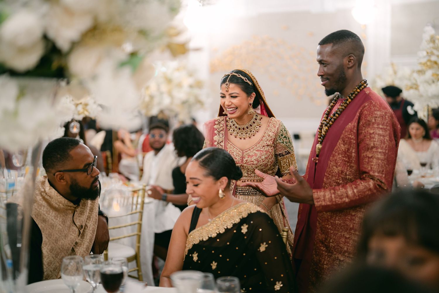 Wedding reception scene with guests and attendees in formal attire celebrating at decorated tables.