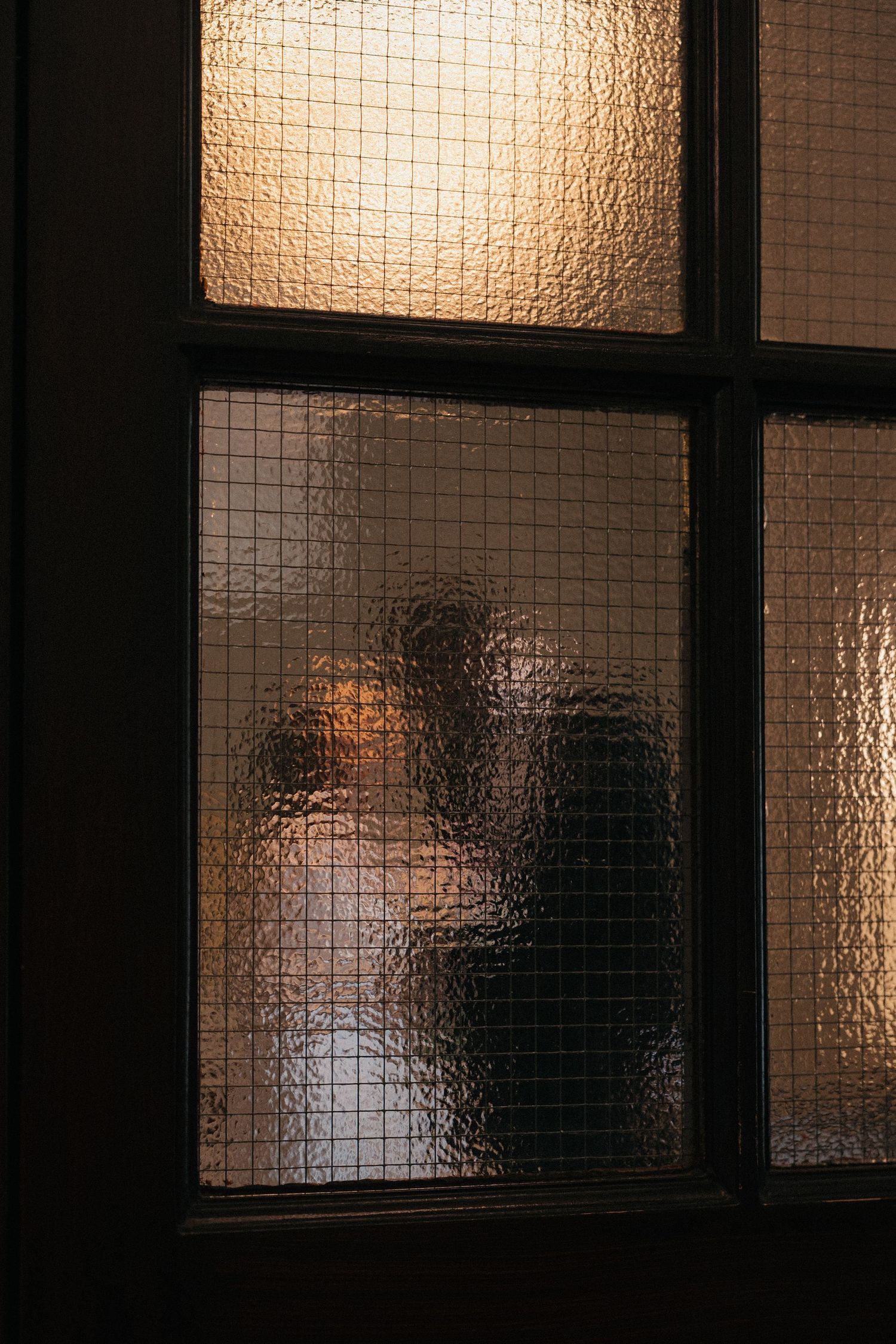 Silhouettes visible through textured glass windows create a dramatic wedding day atmosphere.