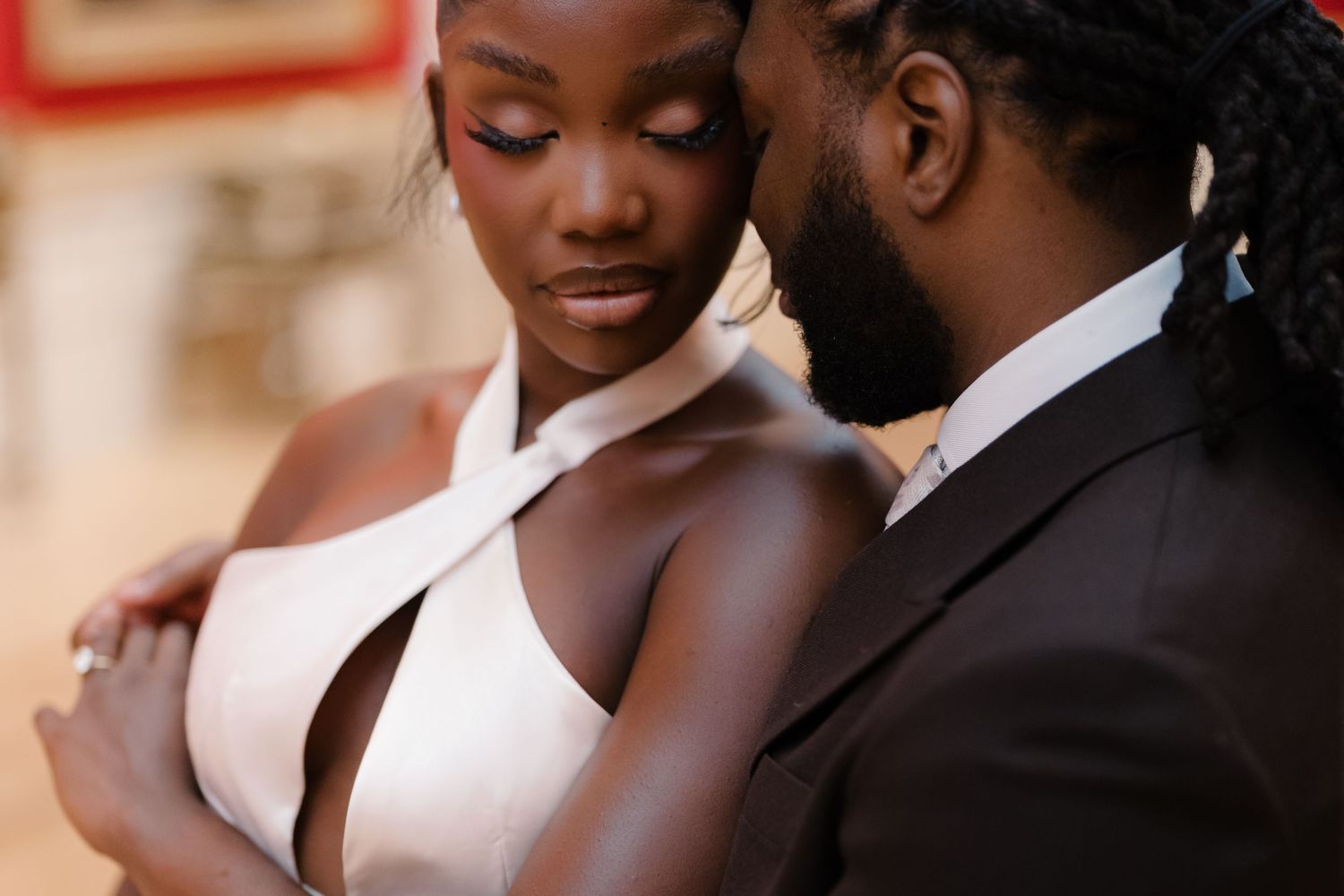 A couple in formal wedding attire share an intimate moment, the bride in a white halter gown and groom in a black suit.