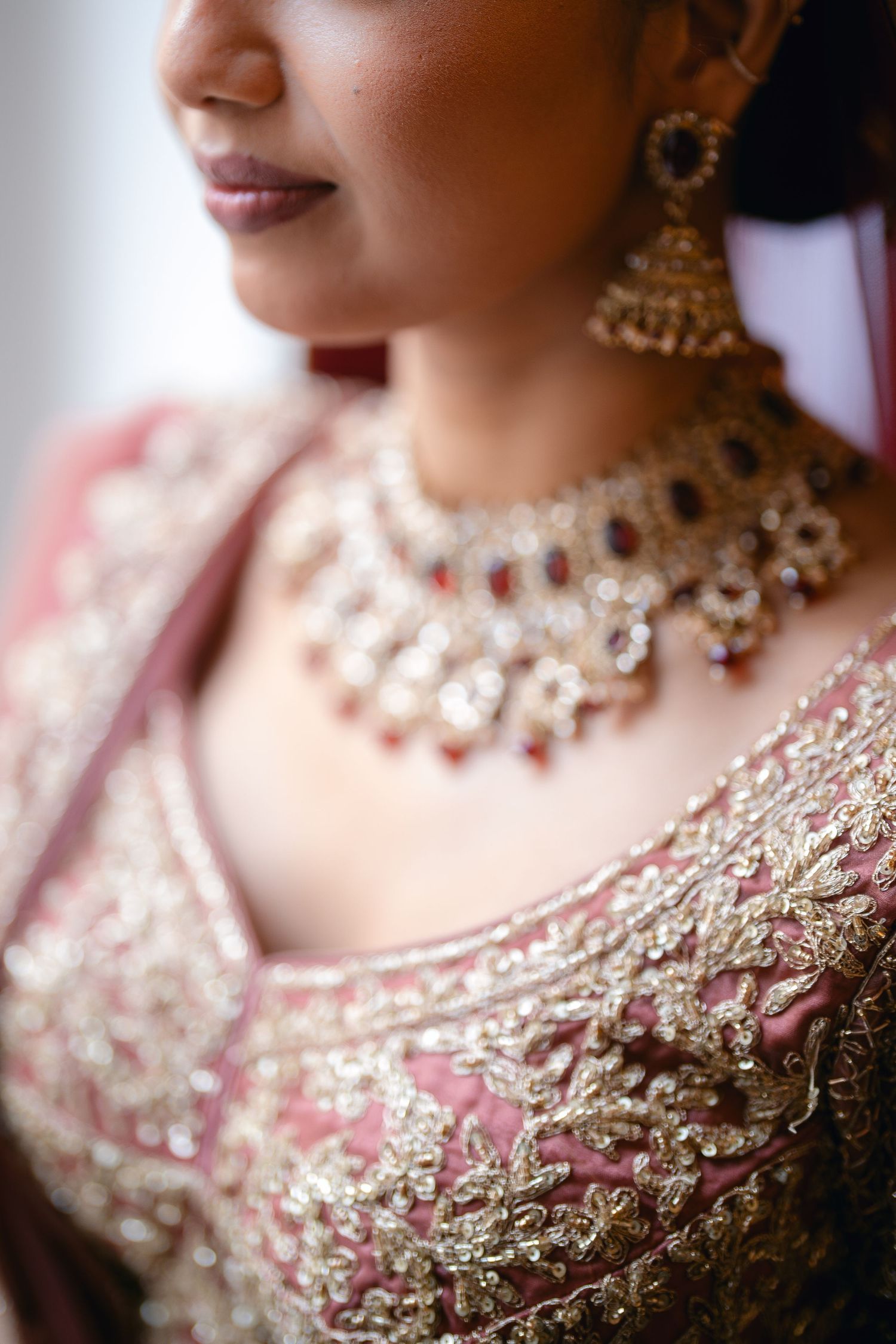 Close-up detail of ornate gold and pink embroidered bridal attire with traditional Indian jewelry.
