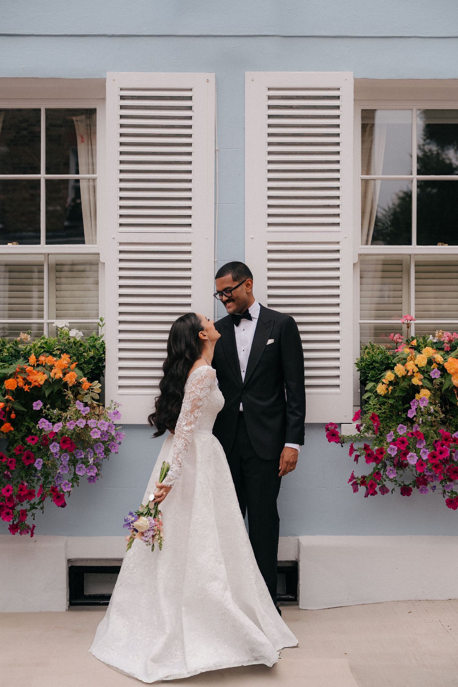 Couple shares romantic moment by window with colorful flower boxes.