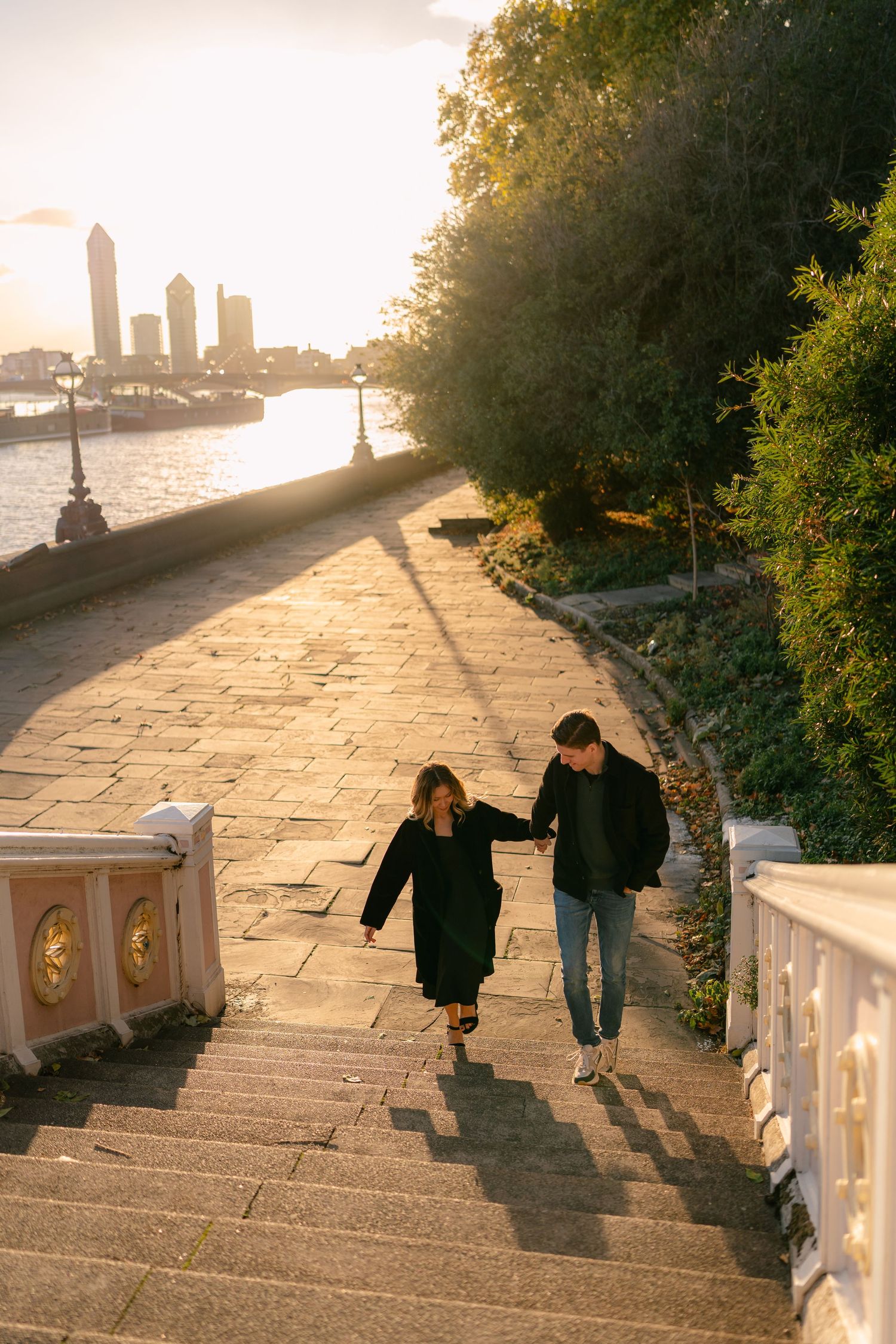 Couple walking down stone steps at sunset with a city skyline in the background.