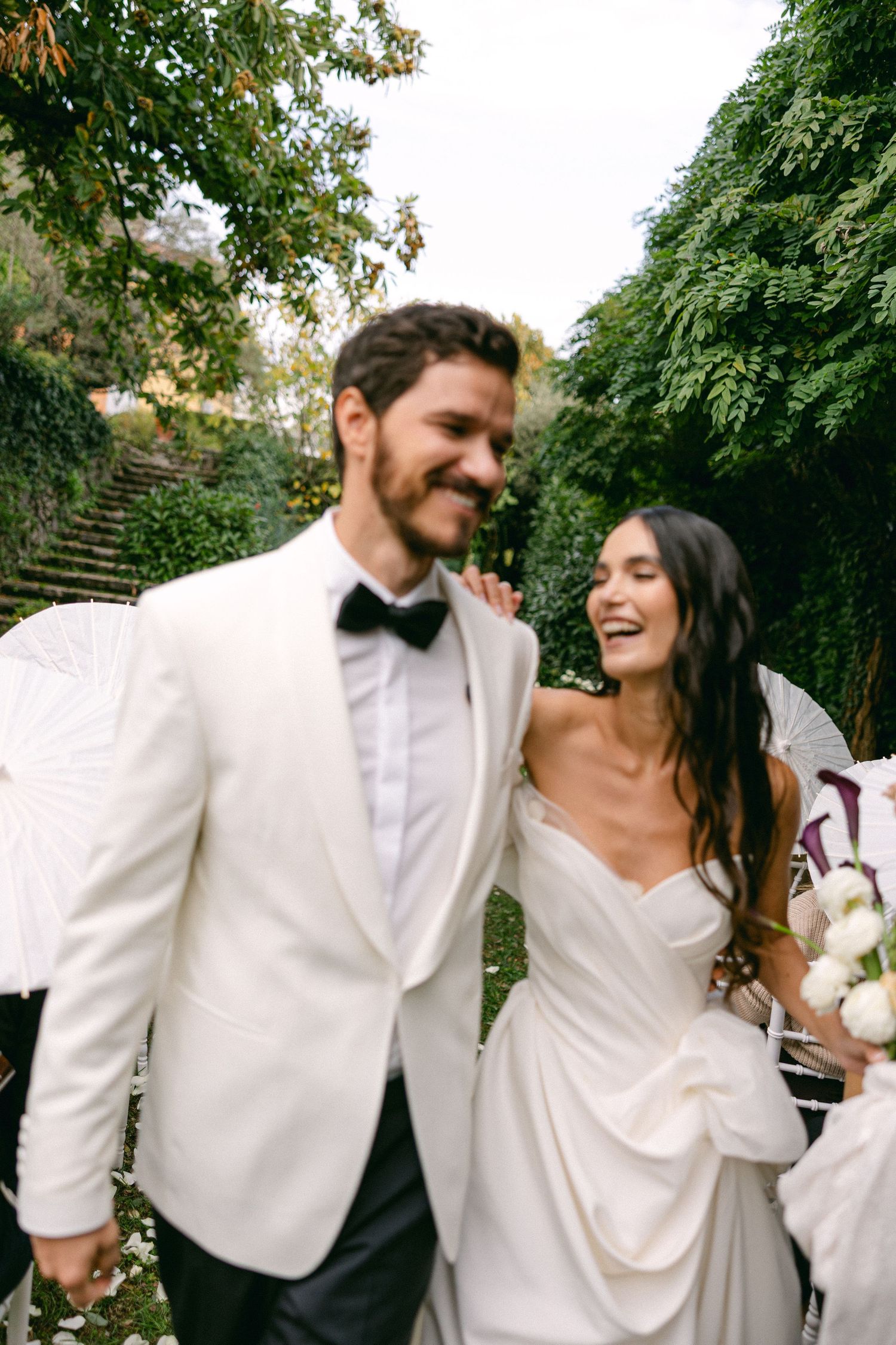 A joyful couple in white wedding attire share candid moments together in a garden setting.