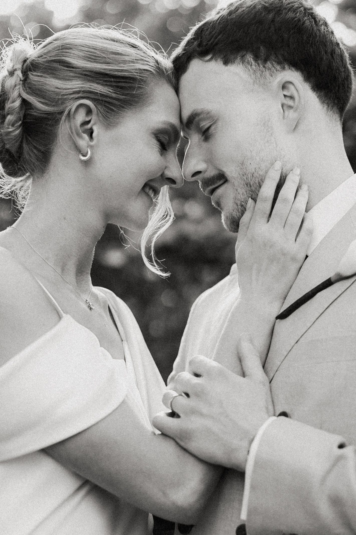 Black and white photo of a smiling bride and groom touching foreheads, sharing a romantic moment on their wedding day.