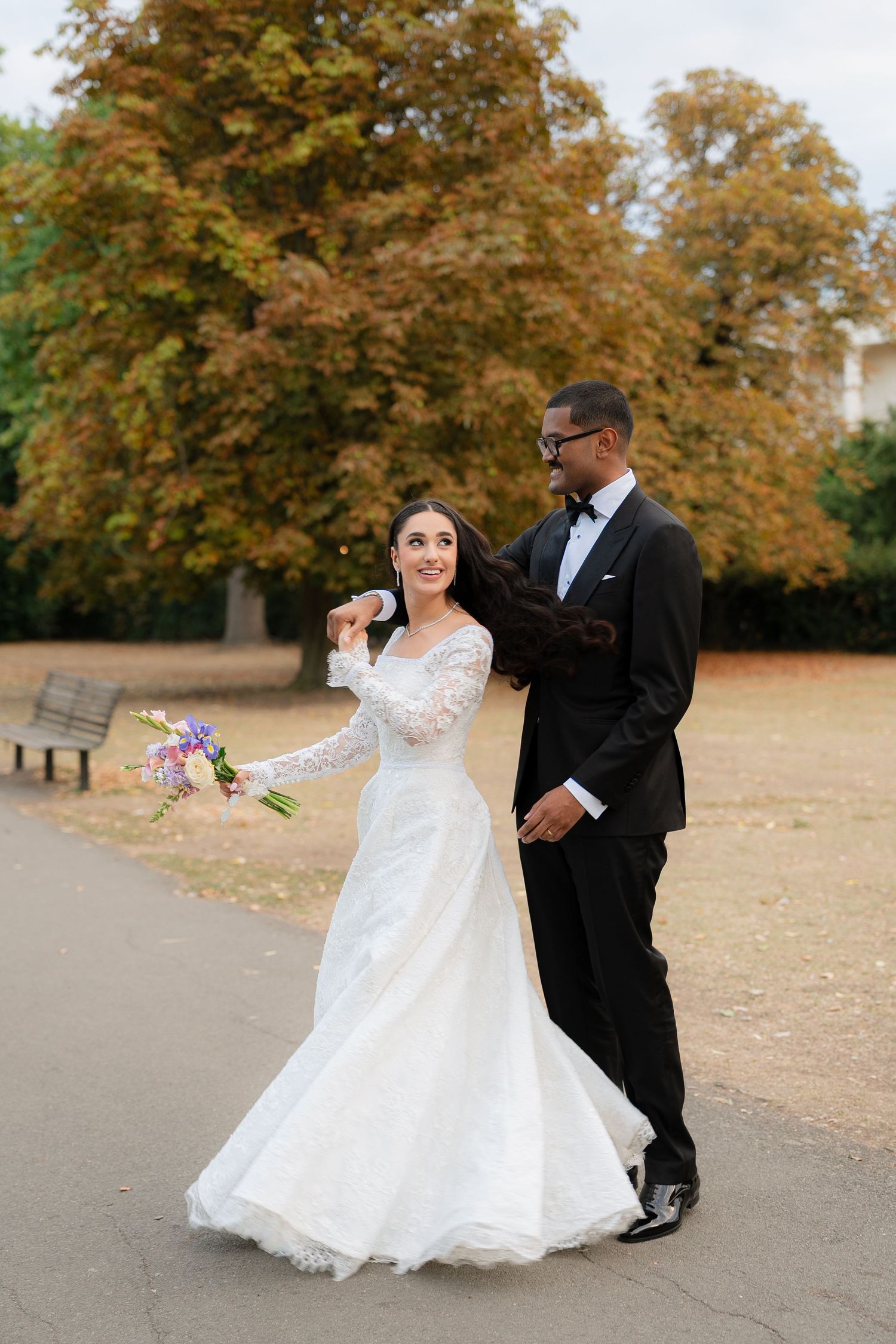 Newlyweds dancing together in a fall setting with autumn trees and colorful leaves in the background.