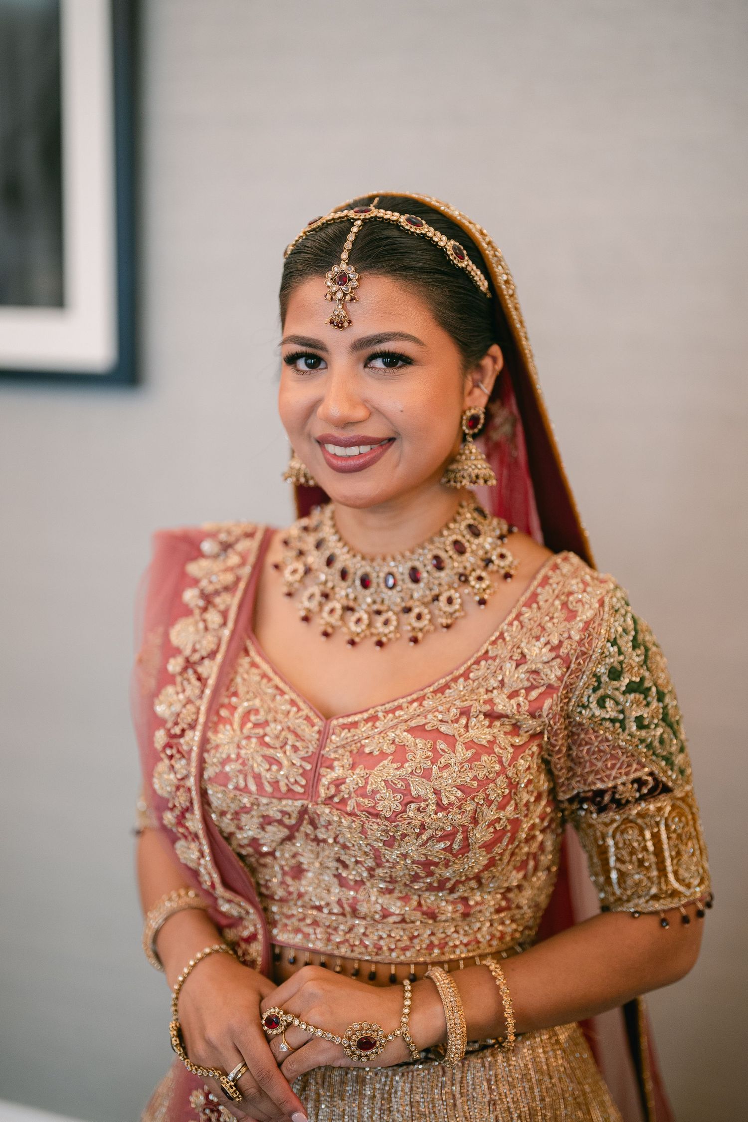 Ornate Indian bridal lehenga in pink and gold with intricate embroidery and traditional jewelry details.