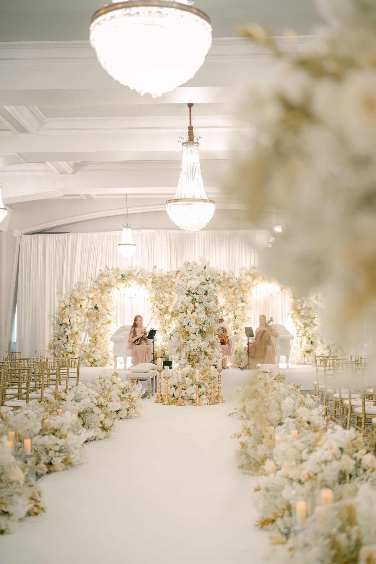 Elegant all-white wedding reception venue with floral arrangements and crystal chandeliers.