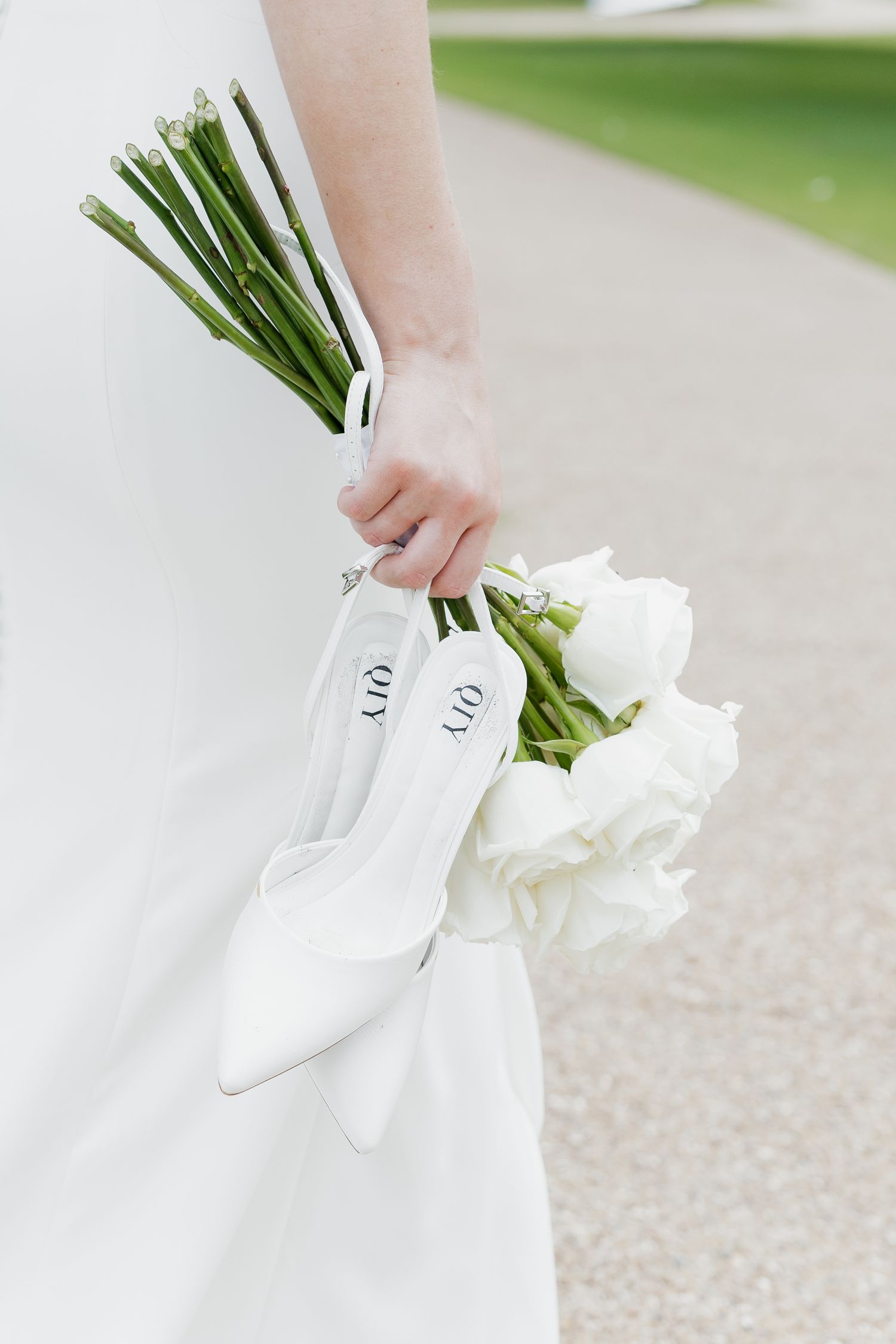 Bride holds white tulip bouquet and Dior wedding shoes in her hand while wearing a white gown.