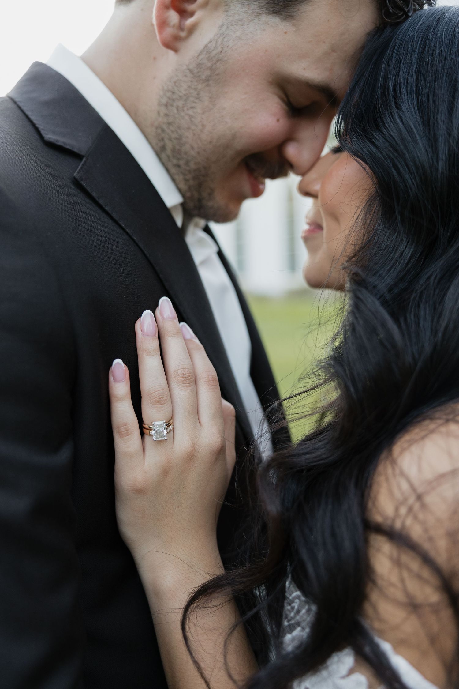 Close-up of smiling bride and groom touching foreheads showcasing large diamond engagement ring.