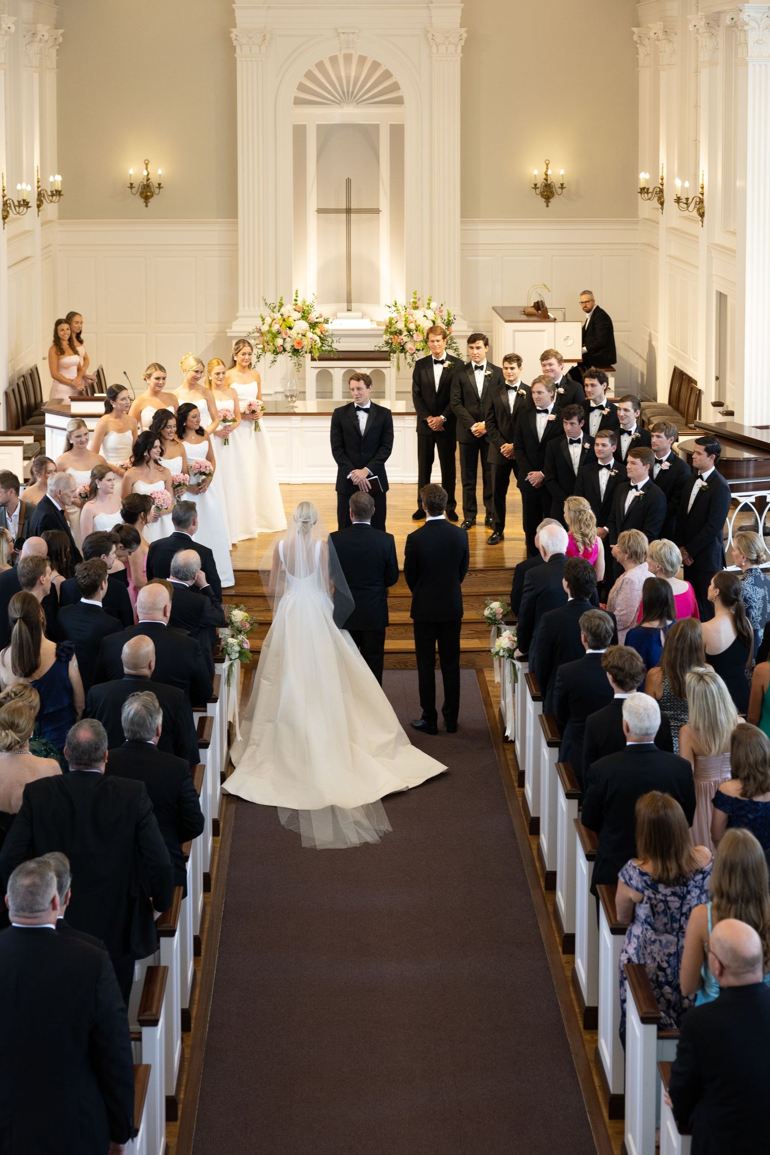 Bride walking down church aisle toward groom during traditional wedding ceremony with full congregation.