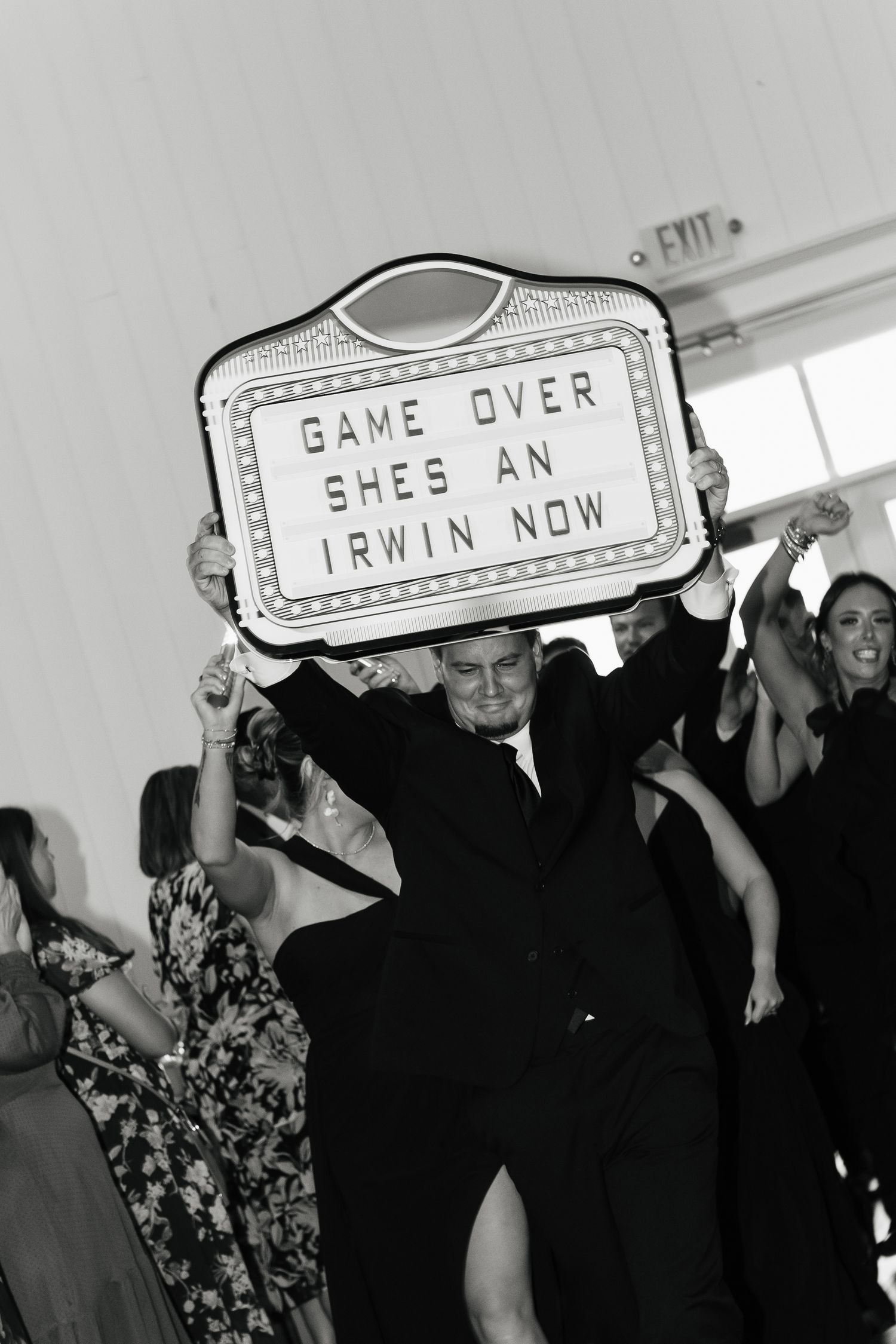 Guest holds marquee sign reading Game Over Shes An Irwin Now at lively wedding reception dance floor.