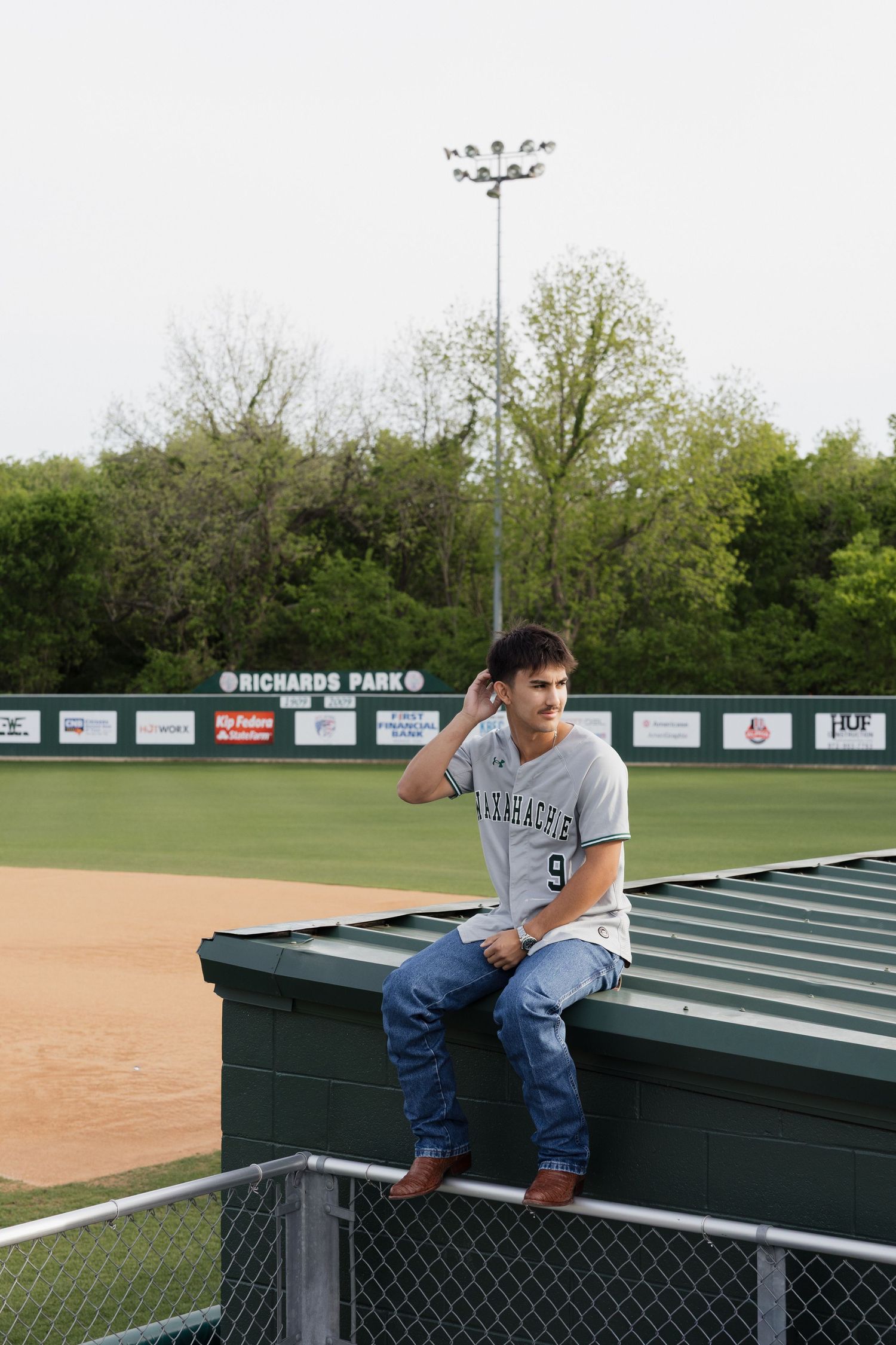 Teen baseball player in jersey number 9 sits on dugout at Richards Park baseball field.