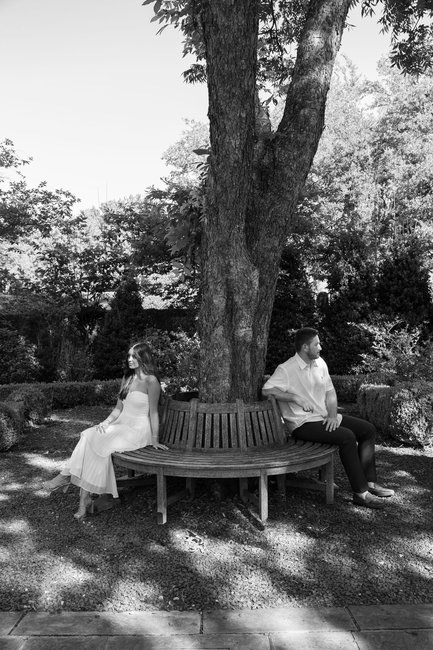 Black and white photo of a couple sitting apart on a circular tree bench in a garden, symbolizing relationship conflict.