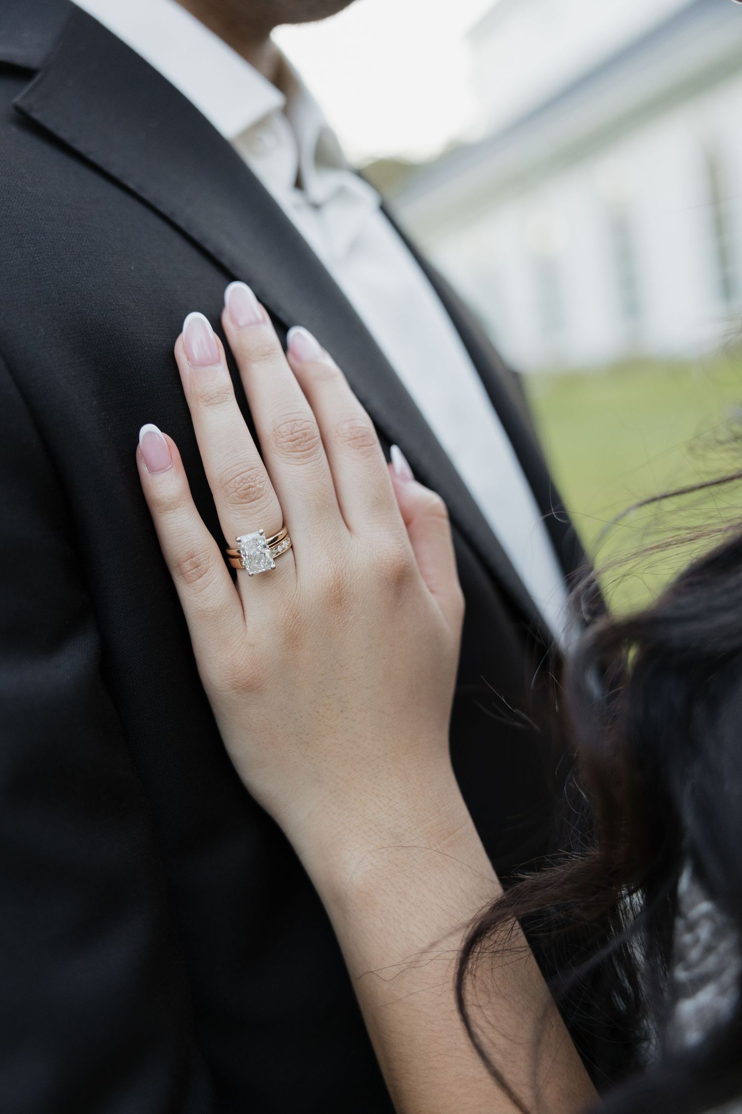 Close-up of bride's hand displaying emerald-cut diamond engagement ring and gold wedding band.