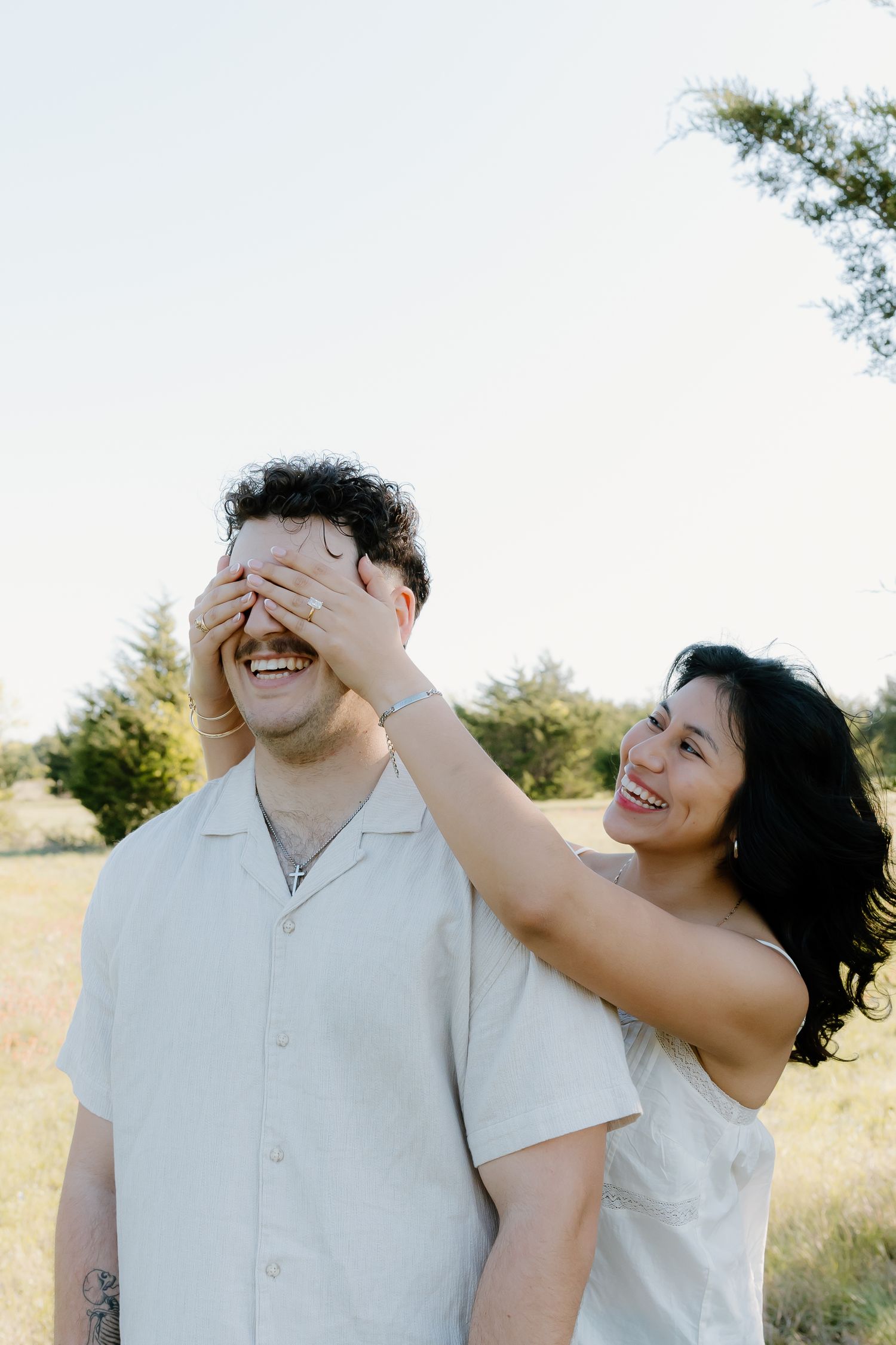 Woman playfully covering man's eyes while both laugh during outdoor engagement session.