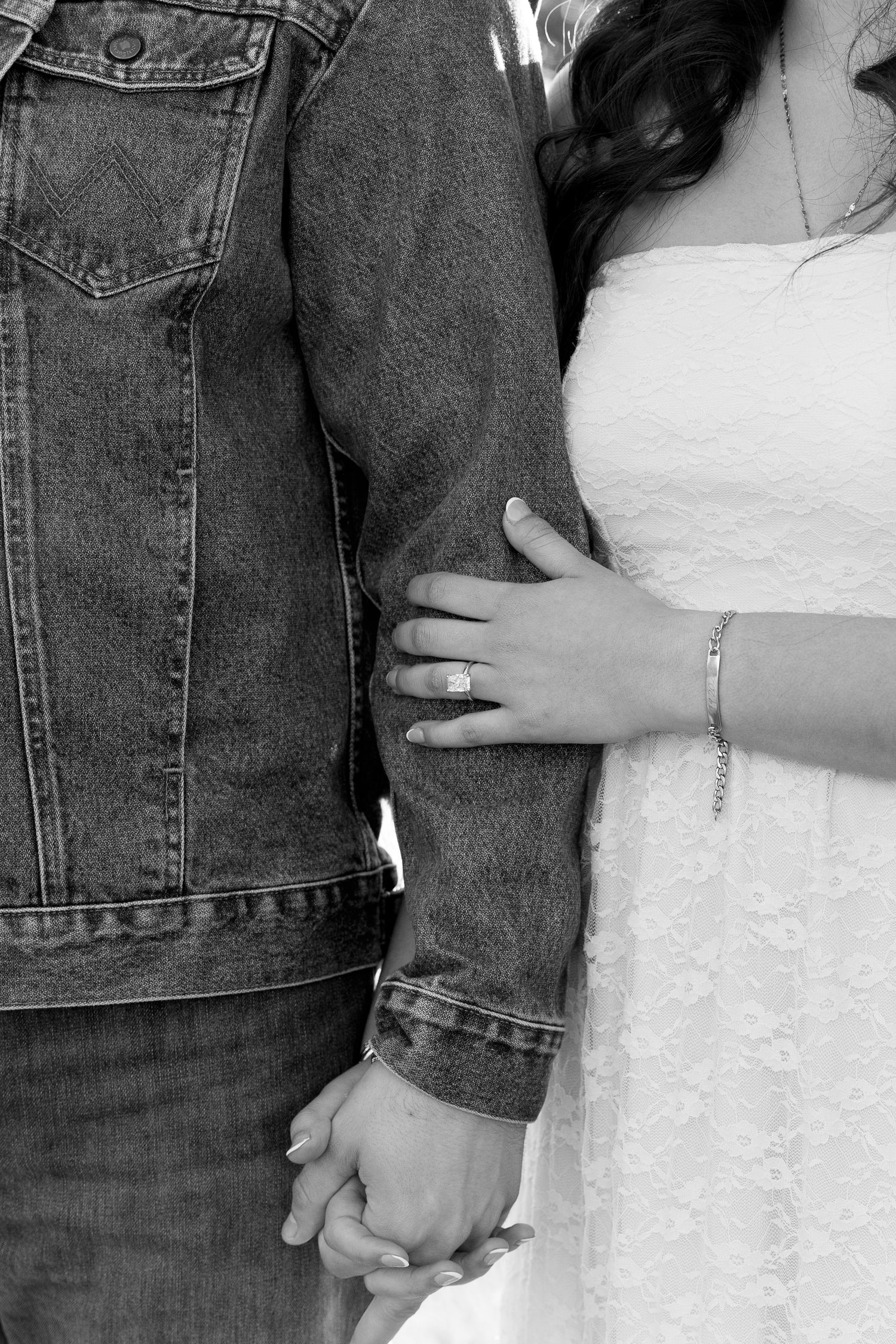 Black and white close-up of engaged couple holding hands showing diamond engagement ring.