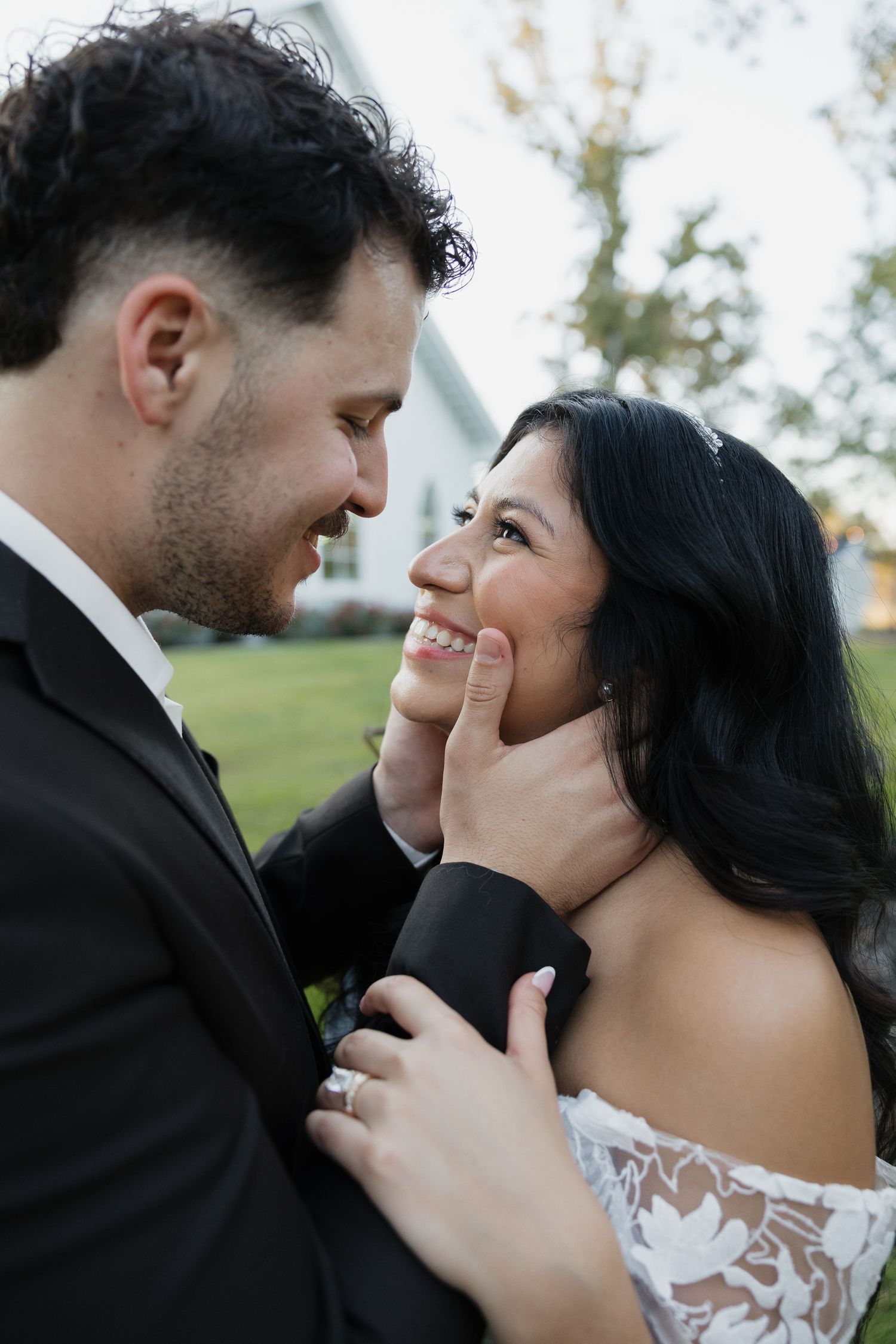 Bride and groom share a tender romantic moment, smiling at each other as groom gently cups brides face.