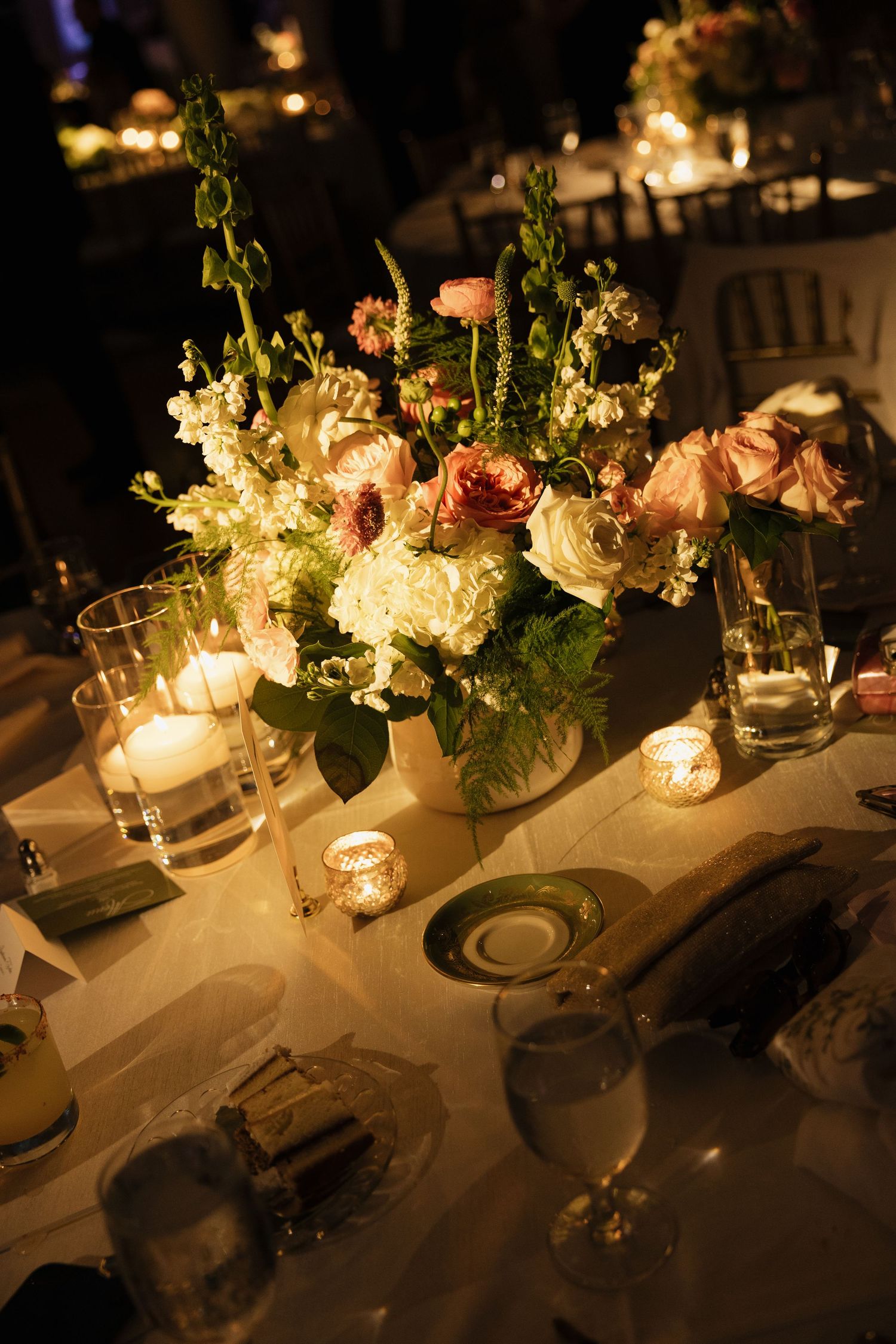 Romantic candlelit wedding reception table with blush and white floral centerpiece arrangement.