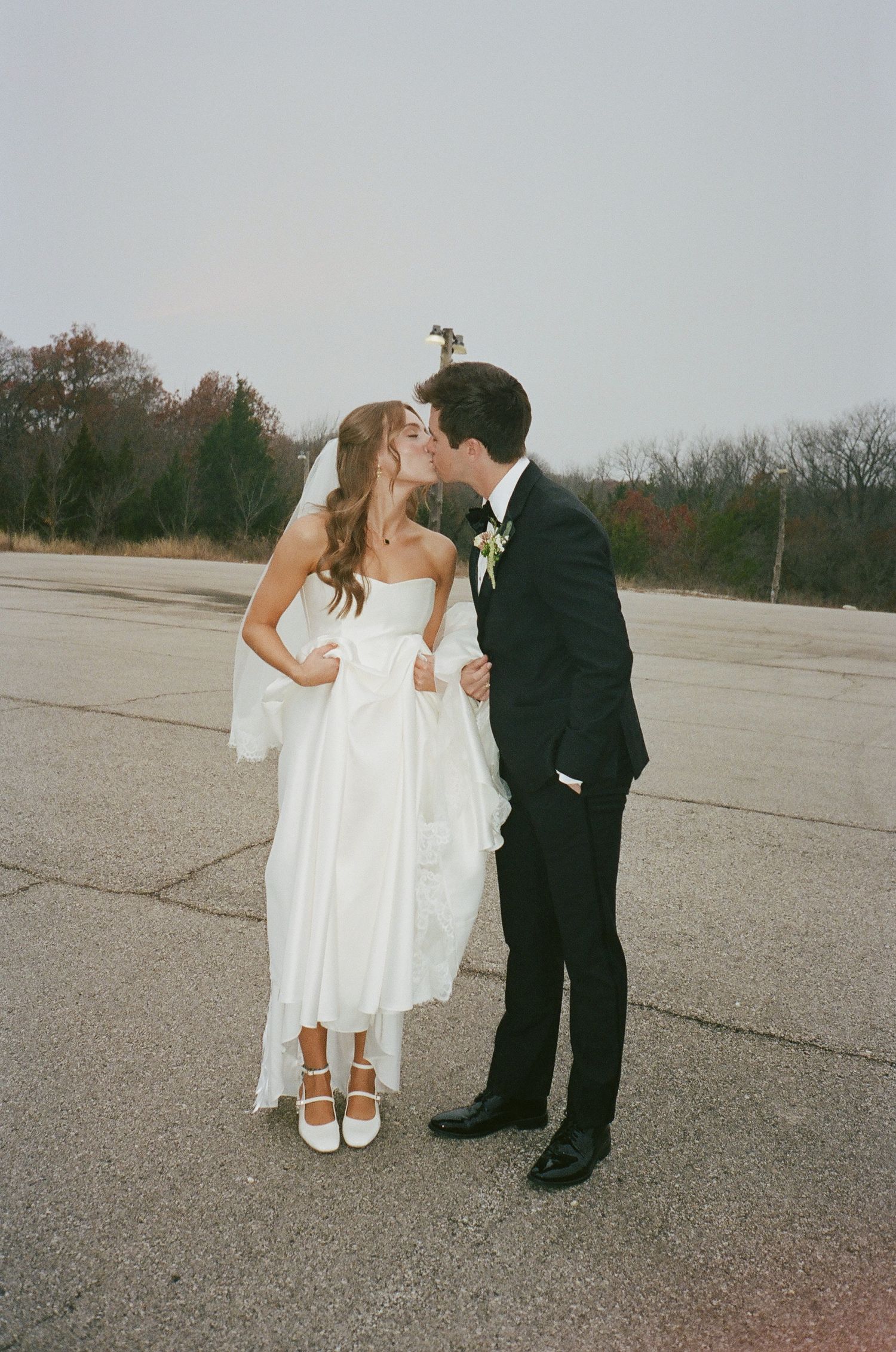 Bride and groom sharing a kiss on open pavement in wedding attire.
