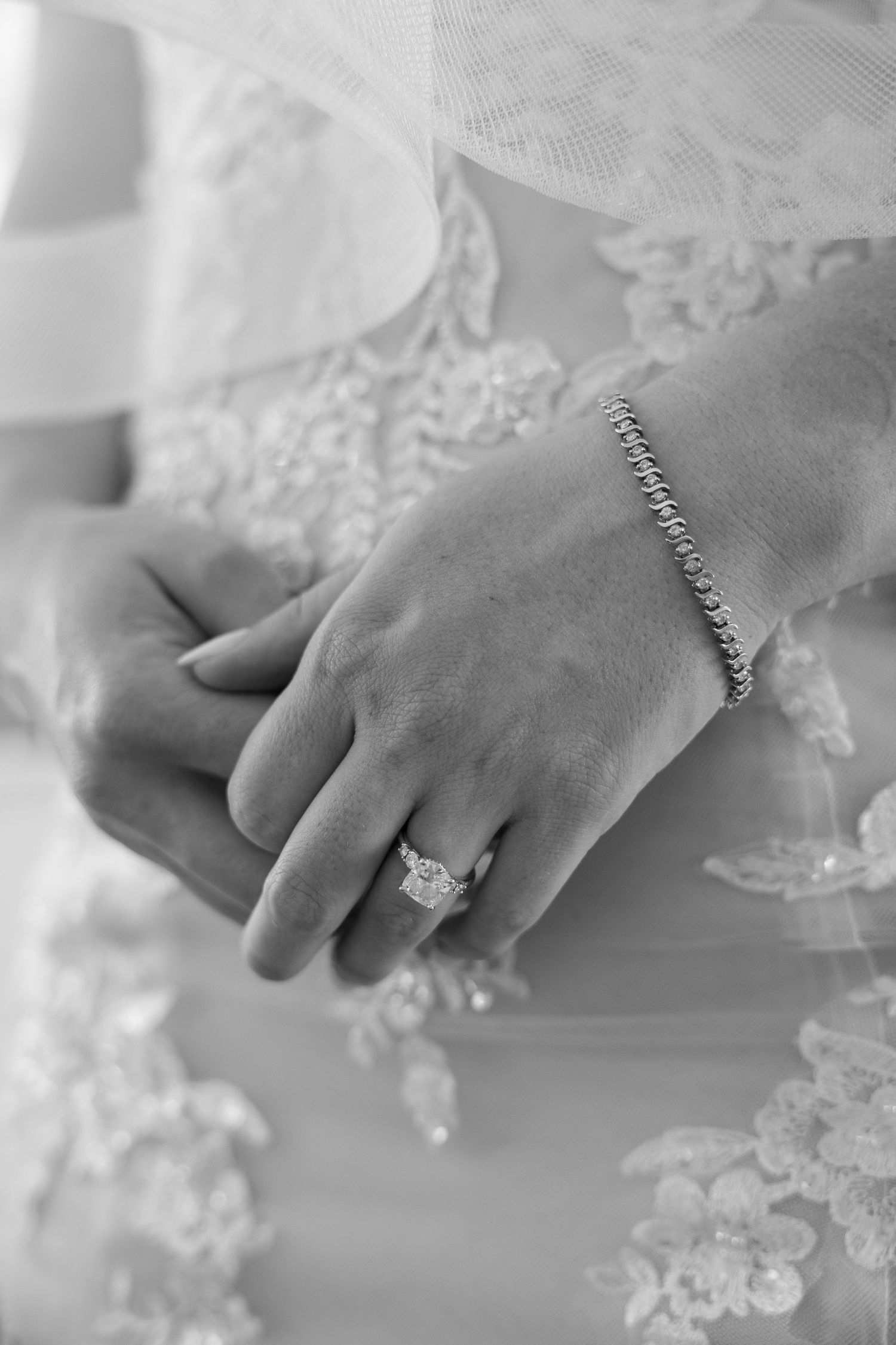 Black and white close-up of bride's hand with diamond ring and tennis bracelet.