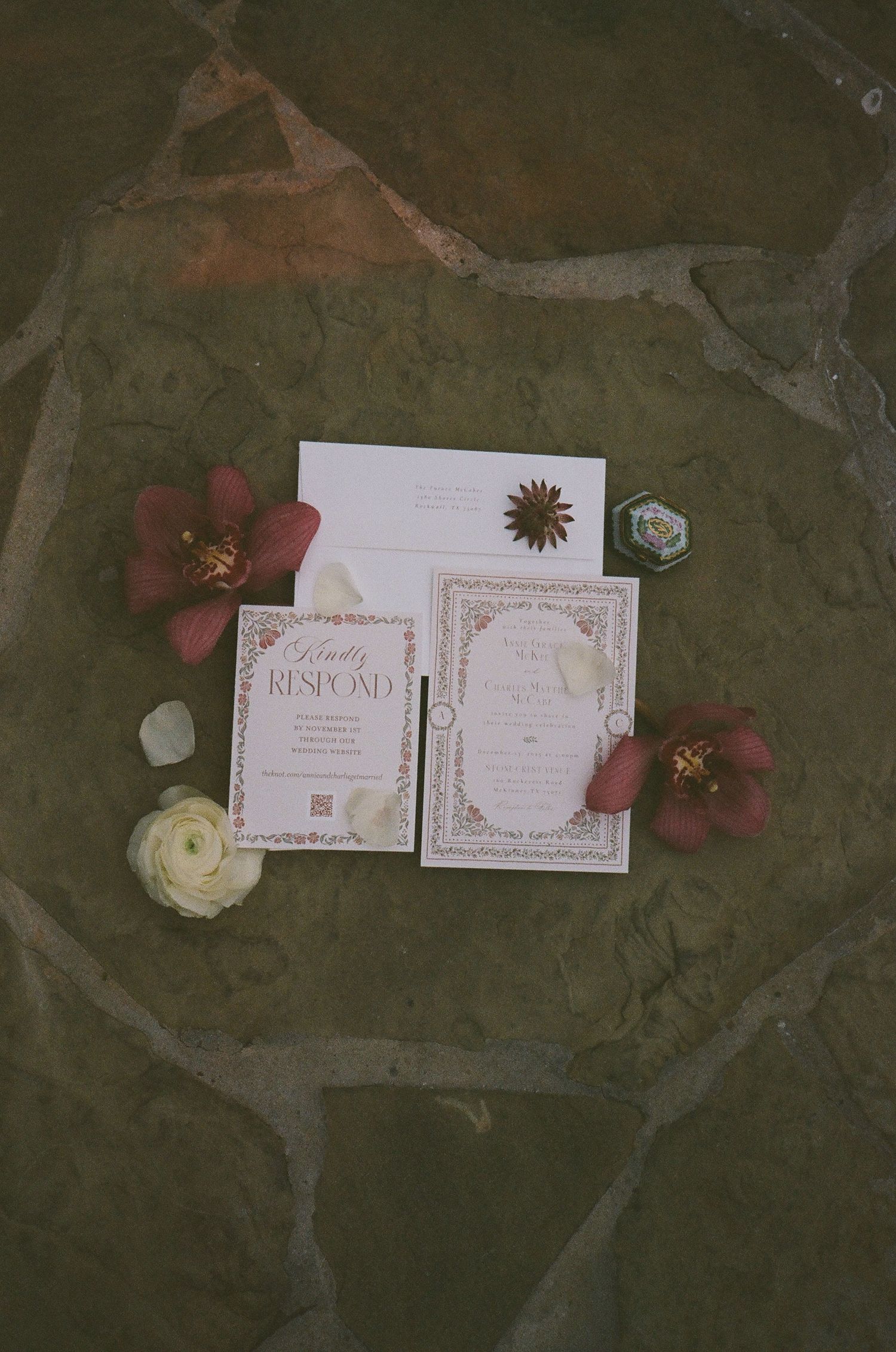 Elegant wedding invitation suite with burgundy floral accents on stone surface.