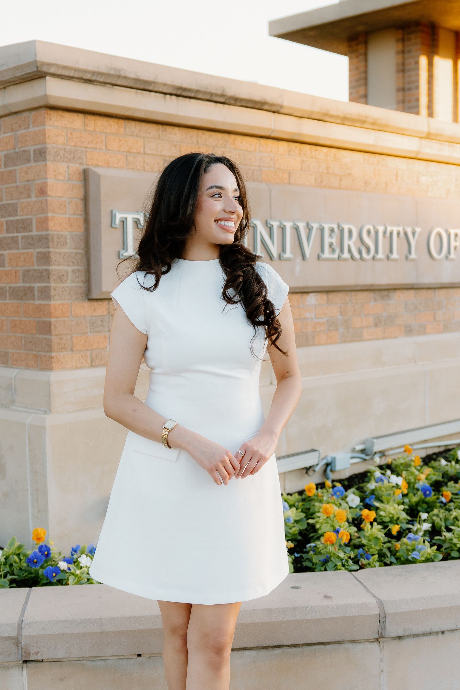 Smiling young woman in white cap-sleeve mini dress standing in front of The University of Texas Arlington sign.