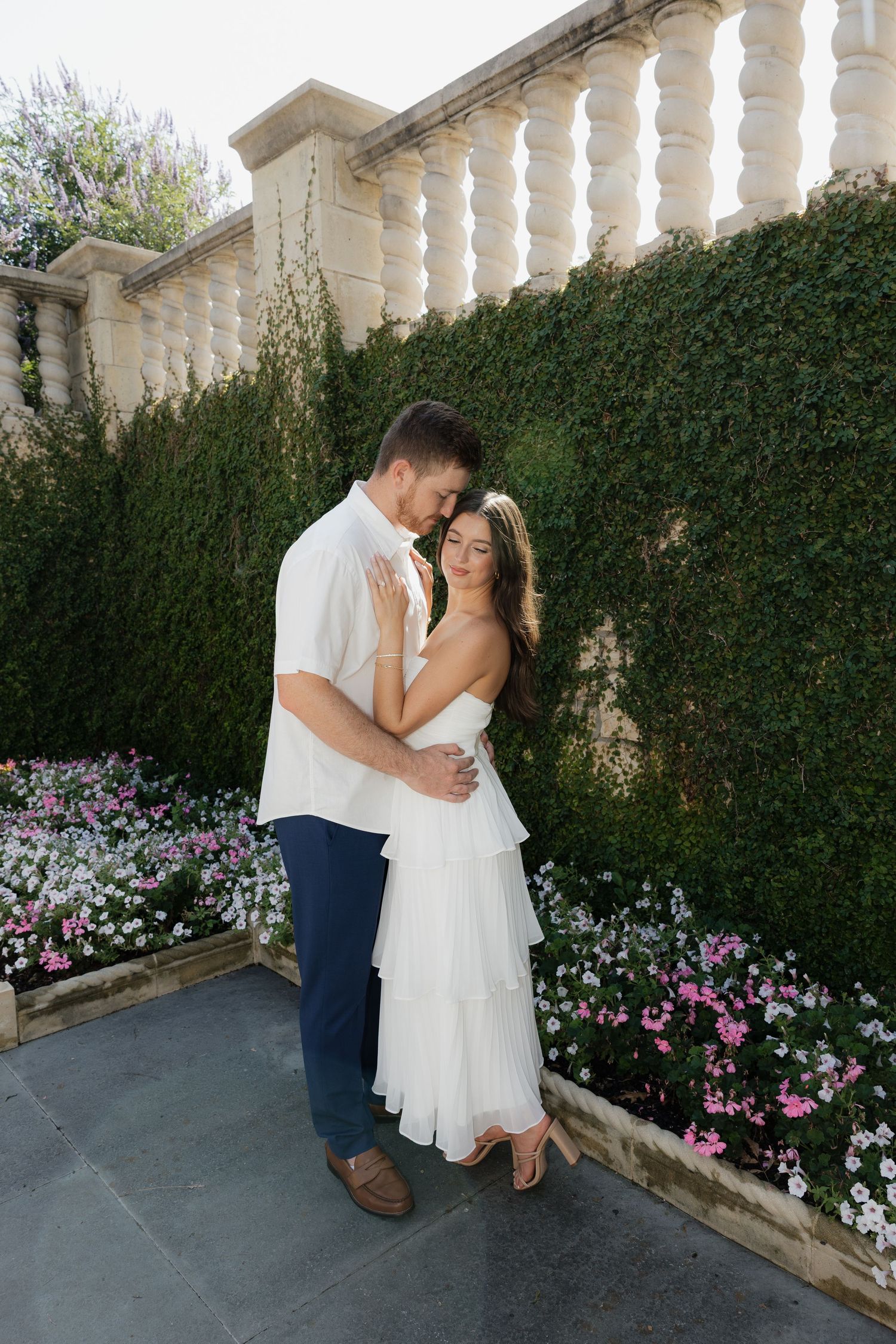 Couple embracing in front of an ivy-covered wall with colorful flowers in a romantic garden.