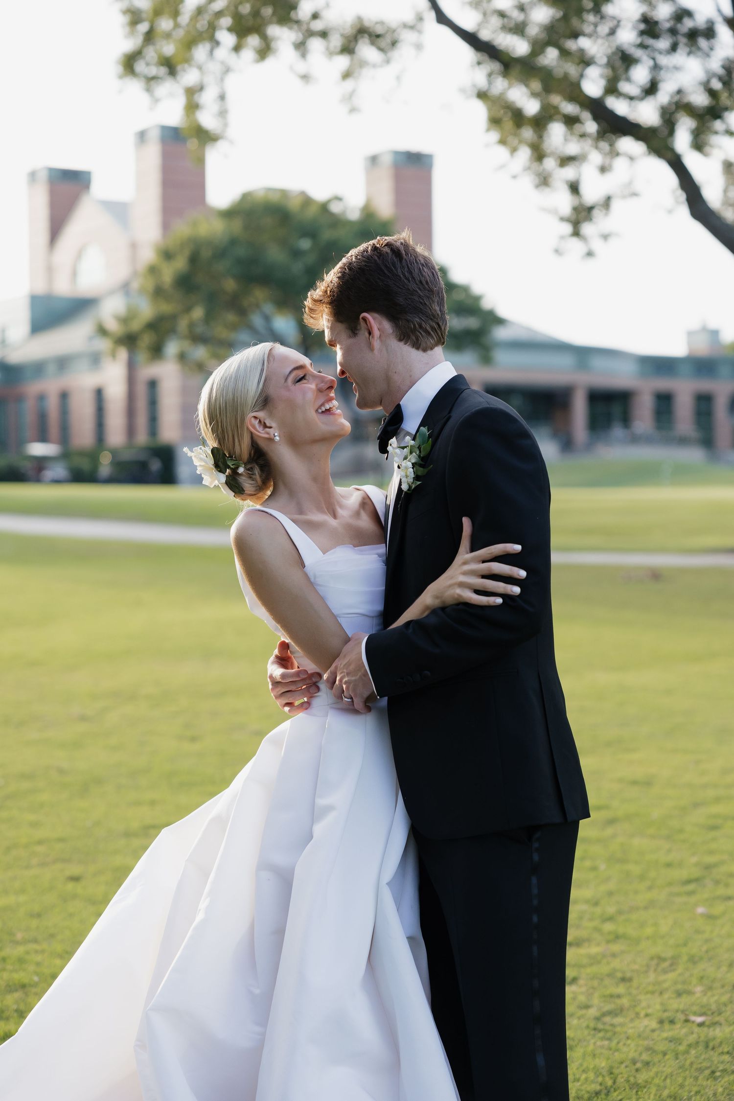 Bride and groom sharing romantic moment on golf course lawn, embracing and gazing at each other at golden hour.