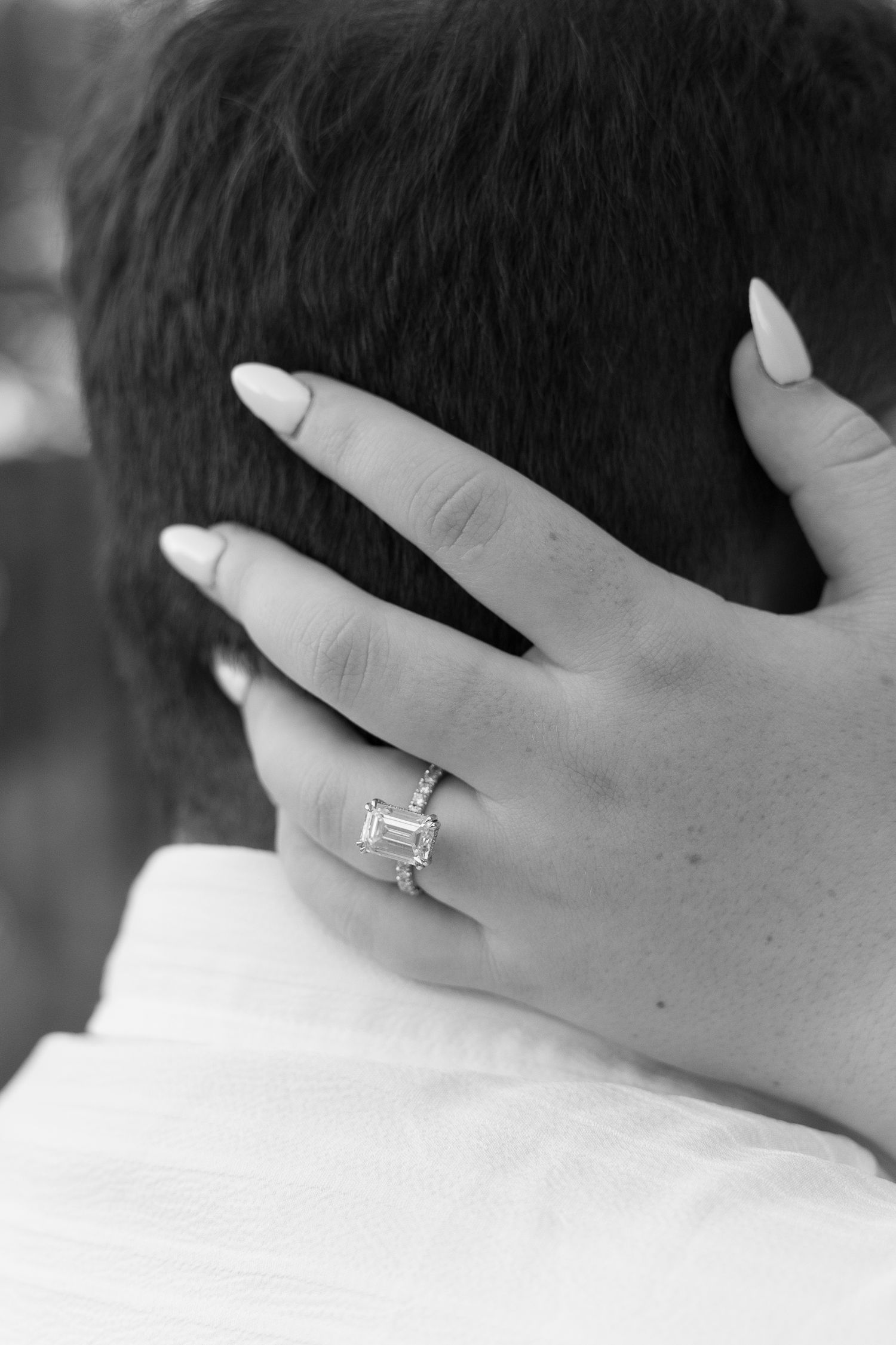 Close-up black and white photo of emerald cut diamond engagement ring on bride's hand.
