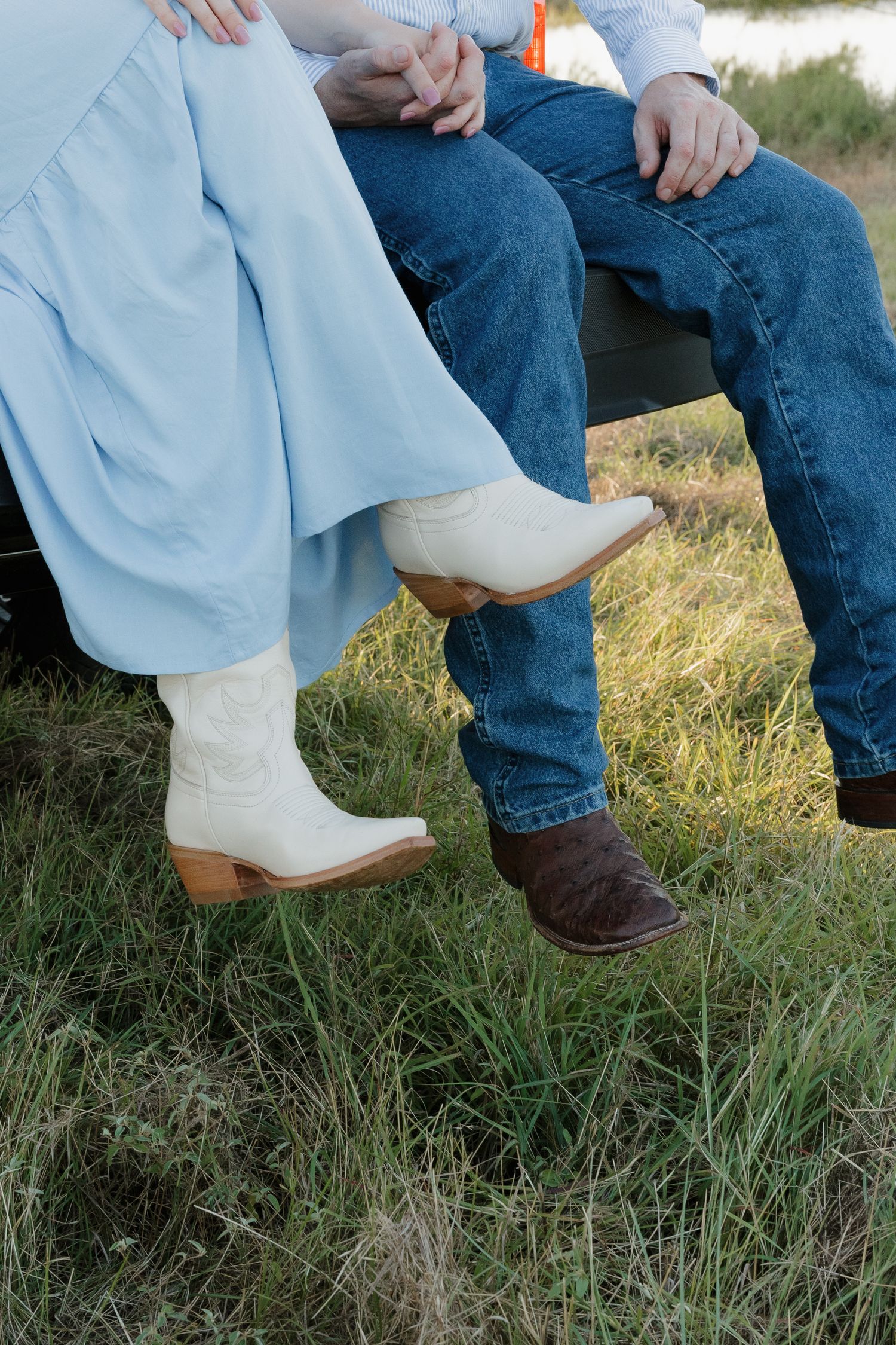 Close-up of couple sitting on a truck tailgate wearing cowboy boots and a light blue dress.