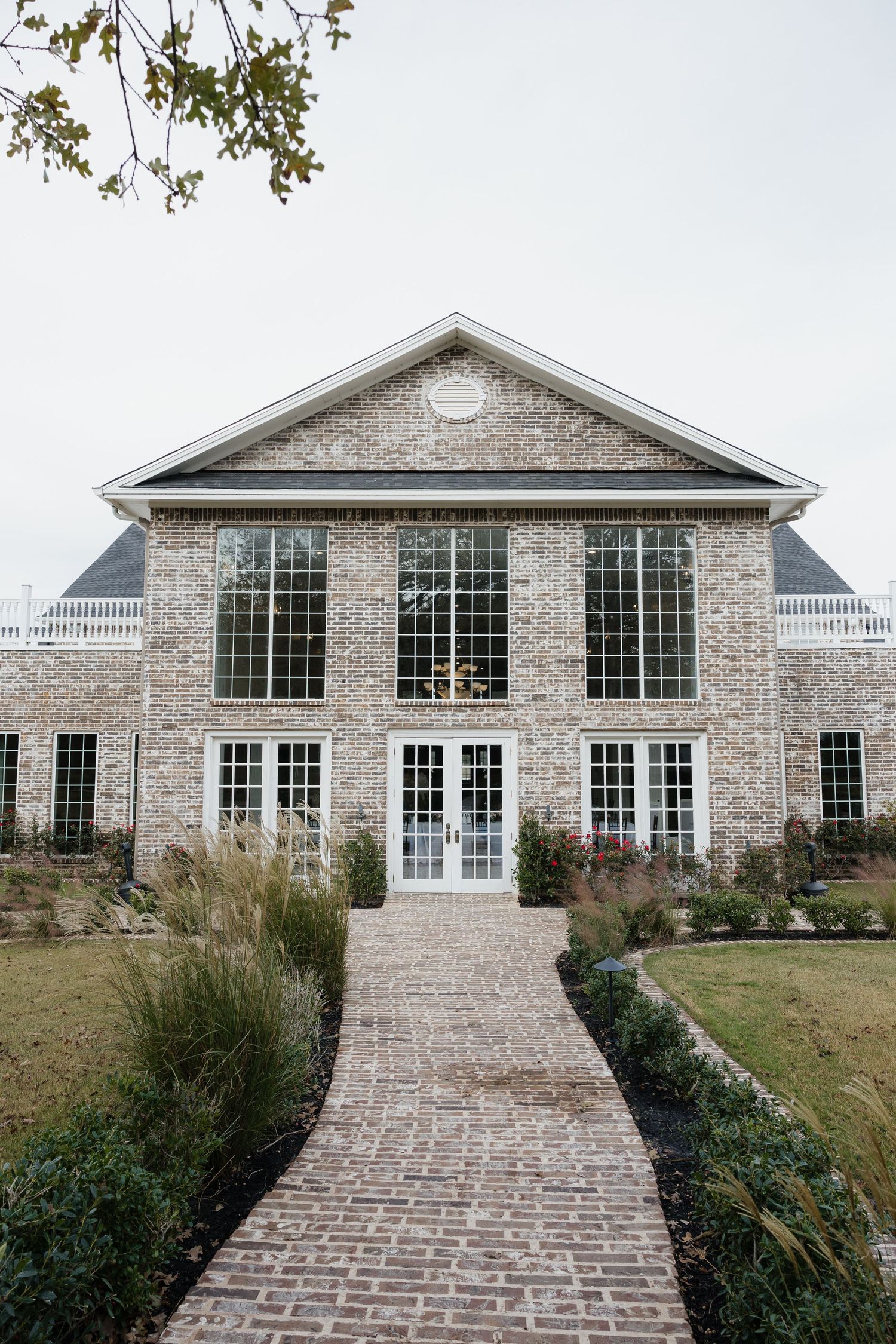 Elegant brick wedding venue with large glass windows and manicured garden along a brick pathway entrance.