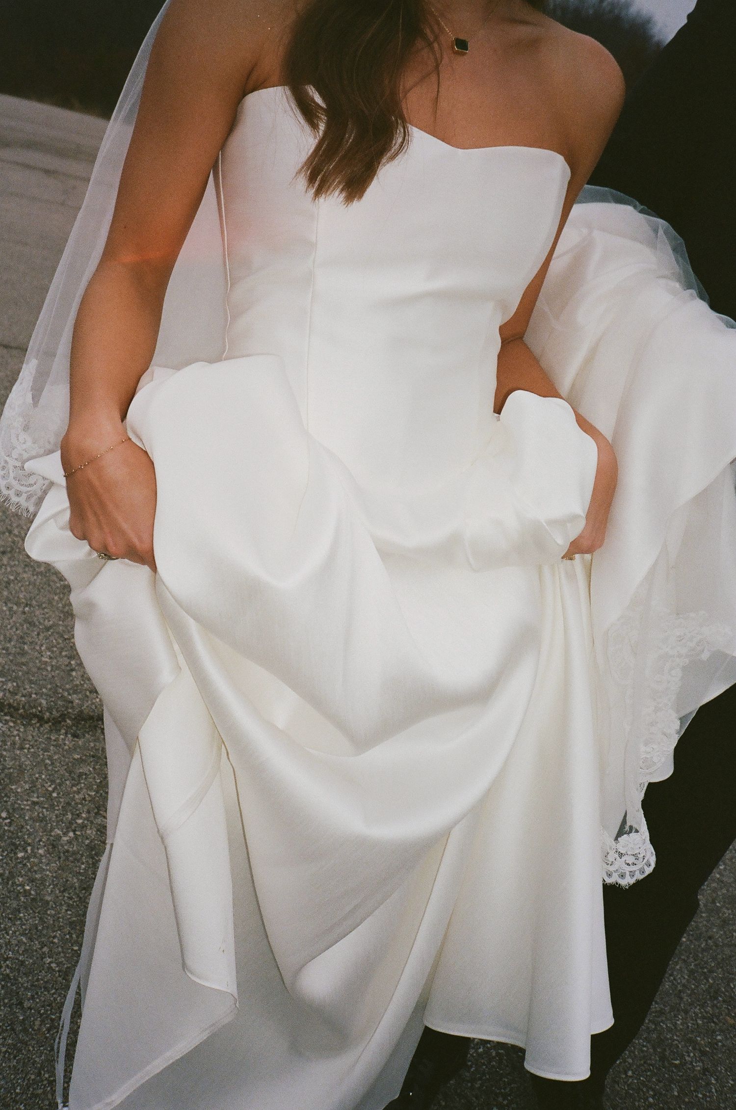 Close-up of bride in strapless white satin gown with lace veil detail.
