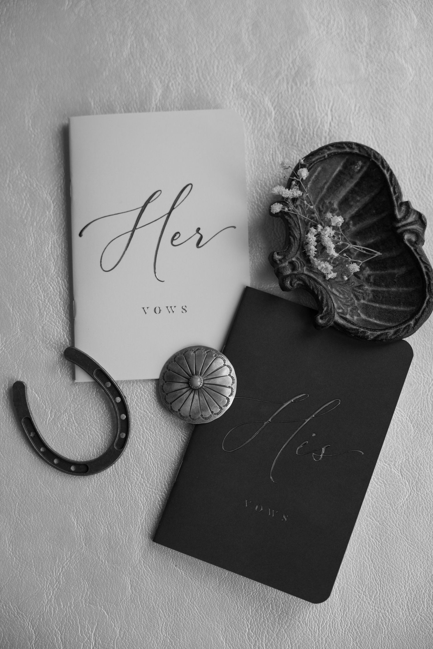 Black and white flat lay of His and Her vow books with horseshoe and vintage accessories.