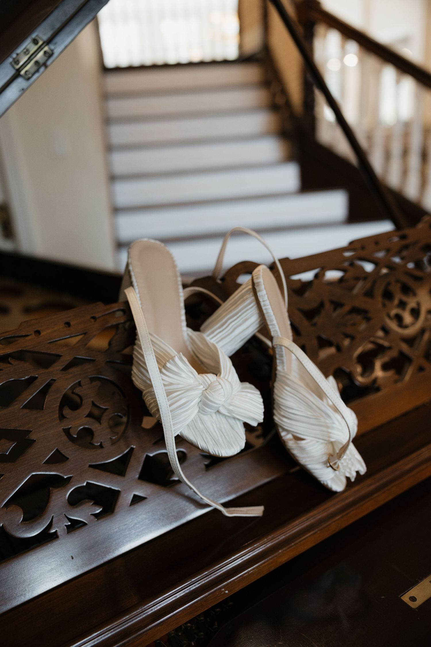 White knotted bow bridal heels resting on ornate dark wood staircase banister.