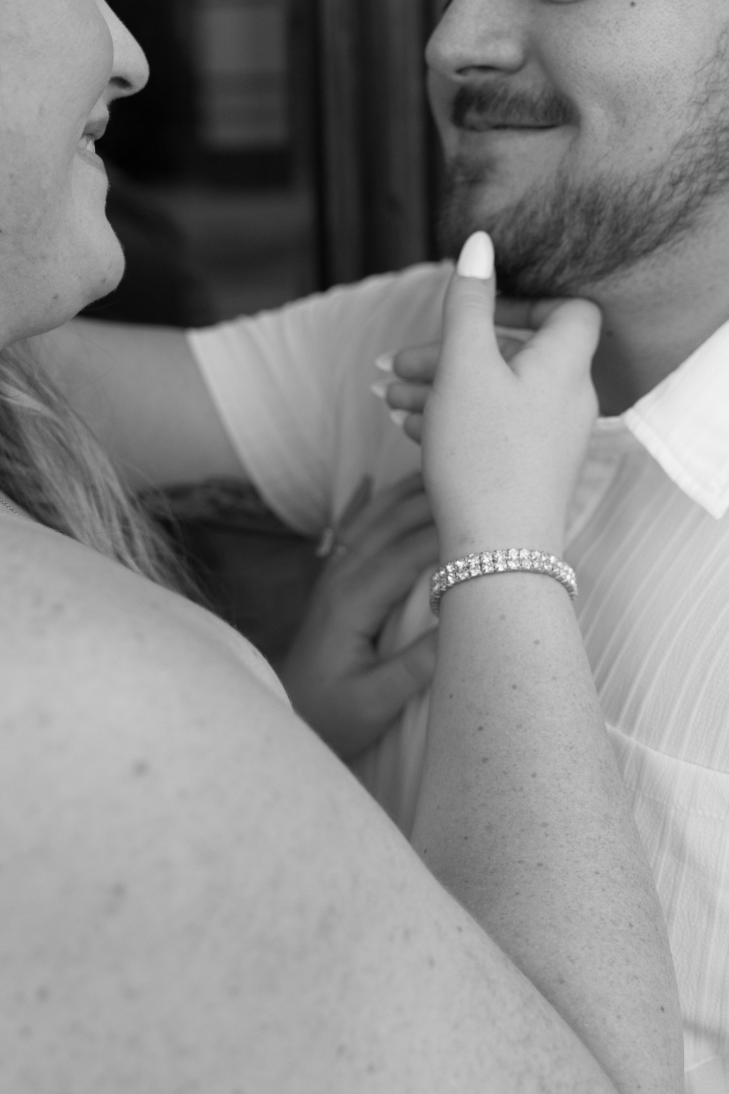 Black and white close-up of a woman touching a bearded mans chin wearing a diamond bracelet.