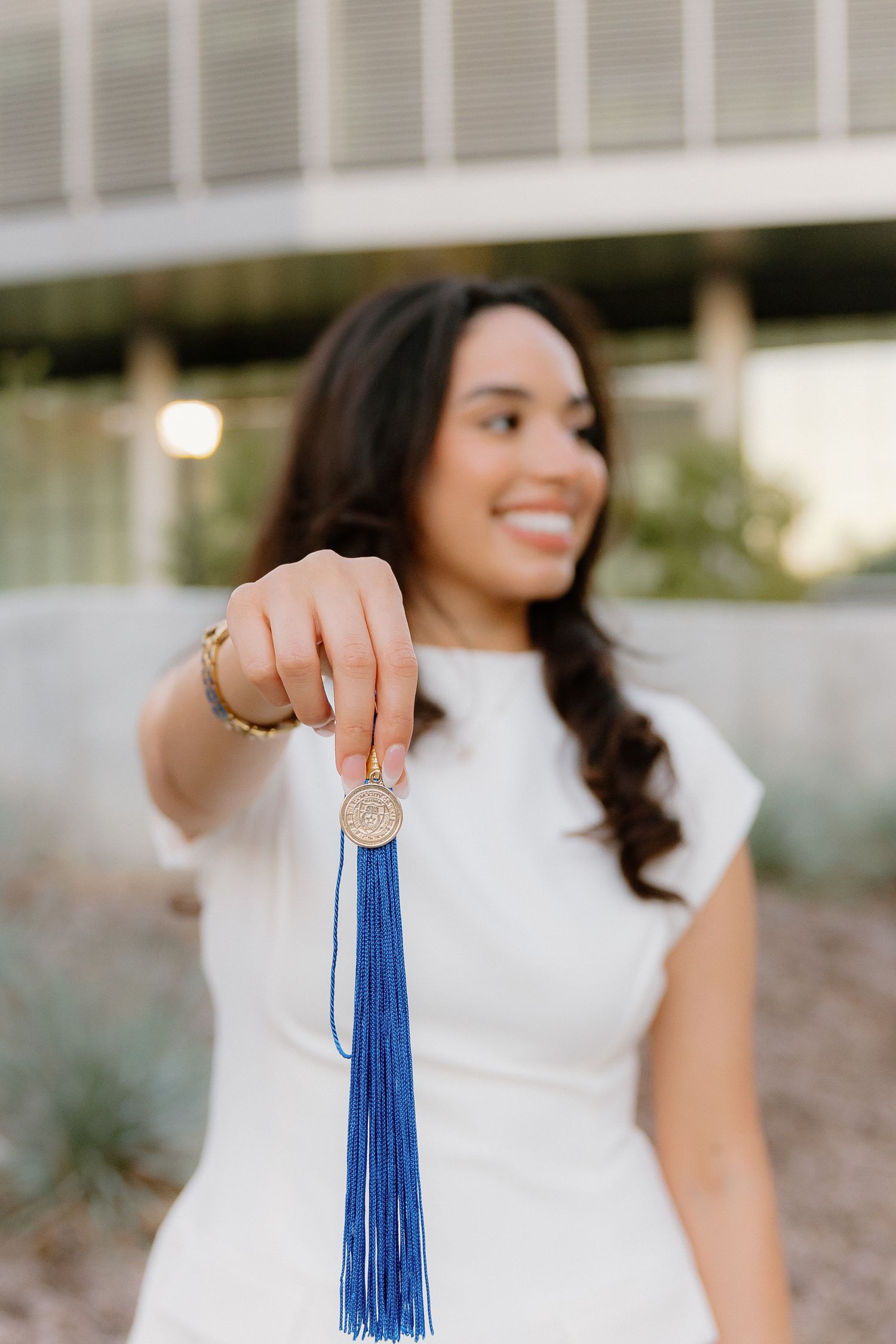 Smiling graduate holding a gold medallion with blue tassel toward the camera.
