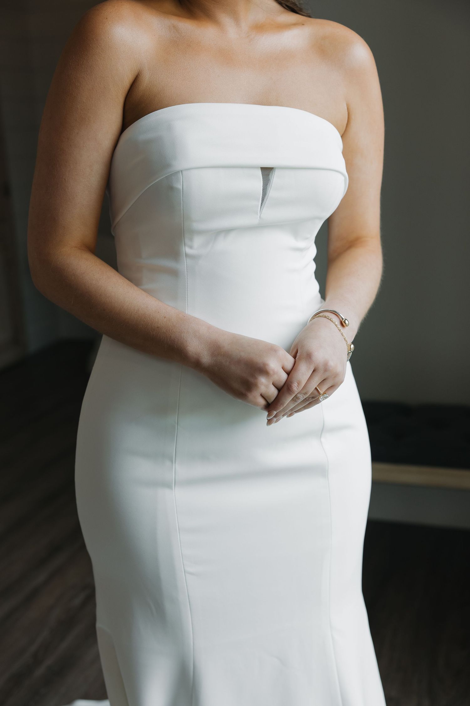 Close-up of bride in minimalist strapless white fitted wedding dress with folded neckline detail.