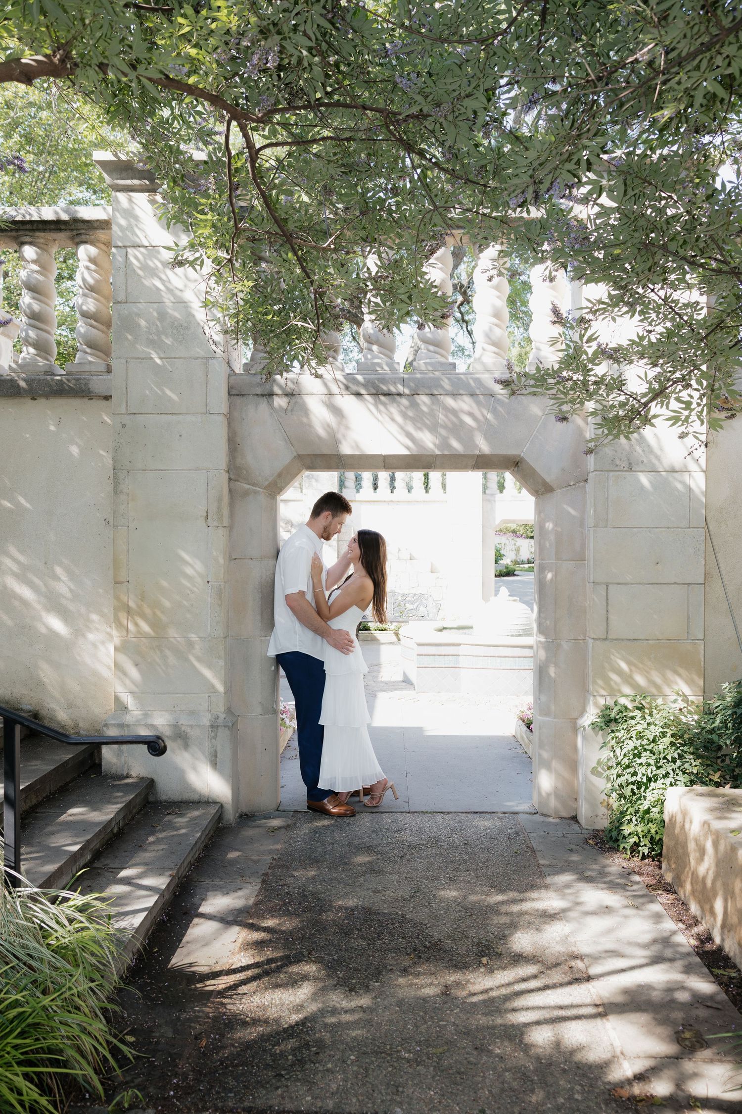 Couple embracing under a stone archway surrounded by lush greenery in an elegant garden setting.