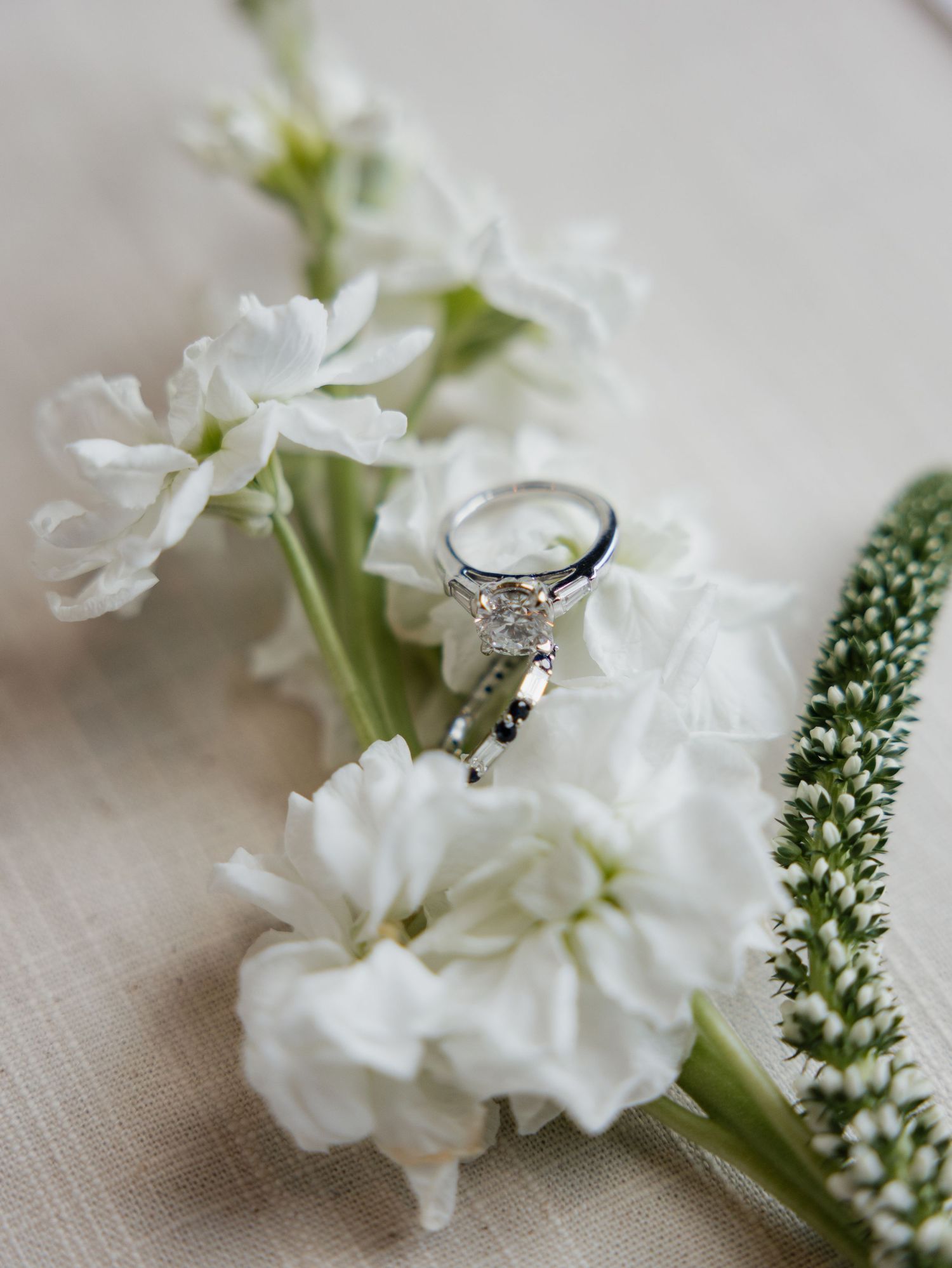 Diamond solitaire engagement ring nestled among white stock flowers and greenery on linen.