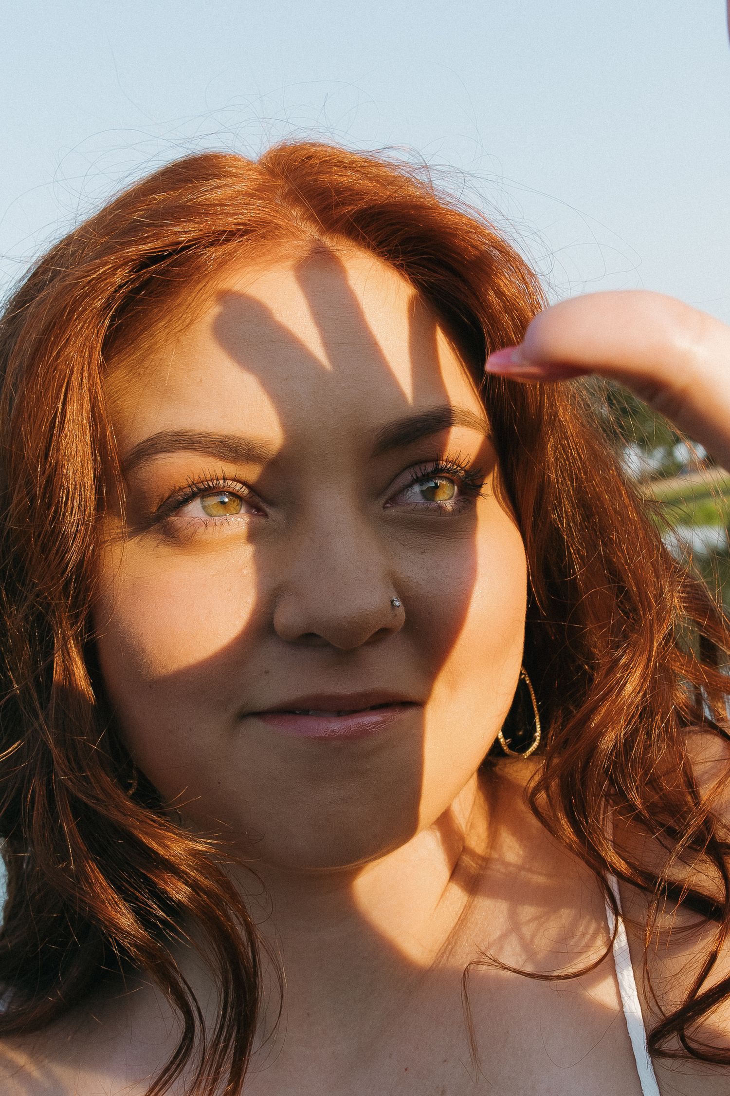 Close-up portrait of a red-haired woman with green eyes and a nose ring with a hand shadow across her face.