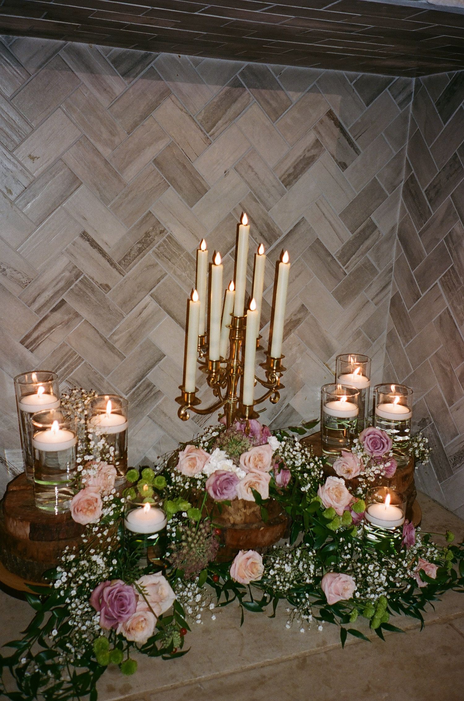 Gold candelabra with white candles surrounded by roses and votives in fireplace.