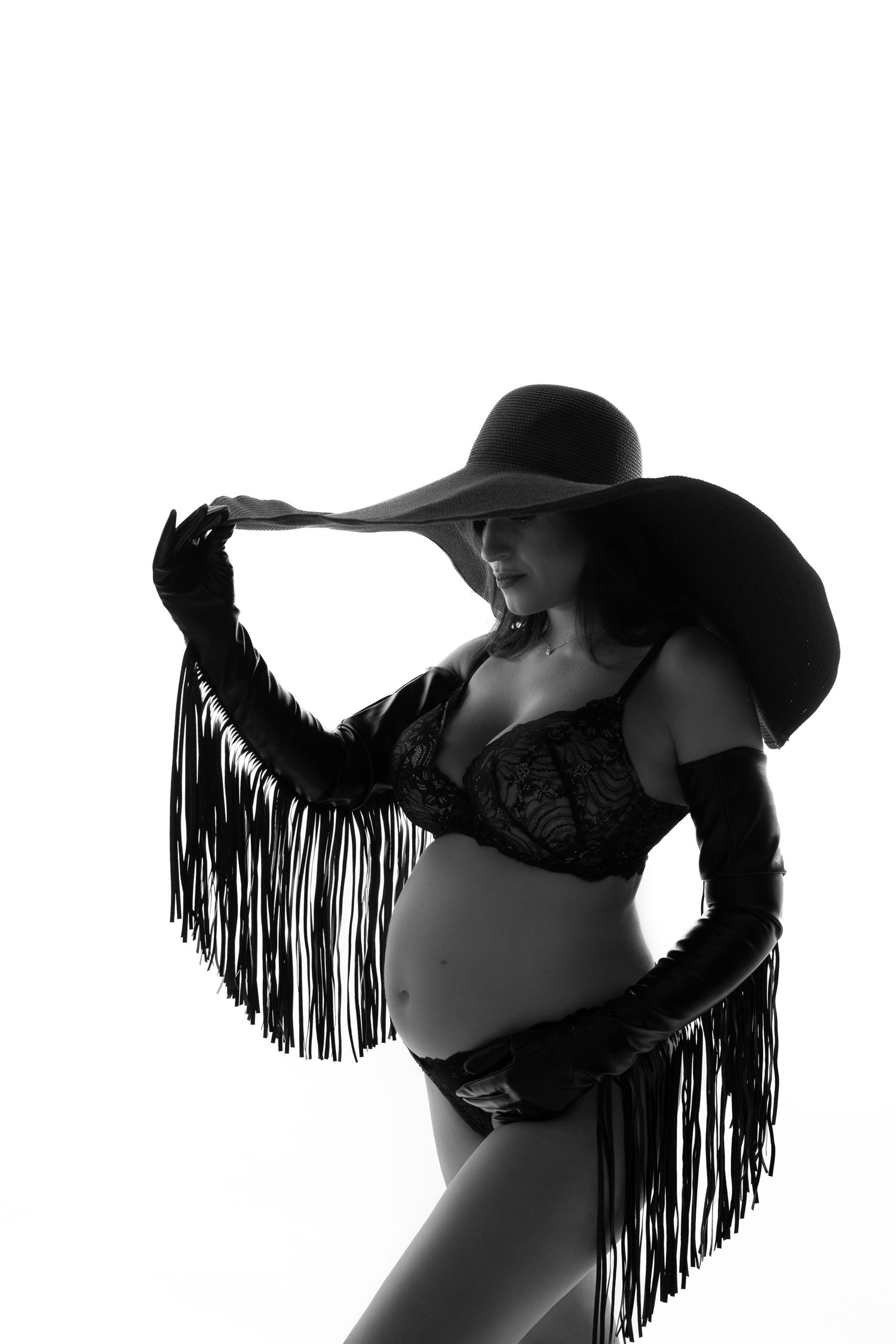 Artistic silhouette of an expectant mother wearing a wide-brimmed hat and fringed accessories.