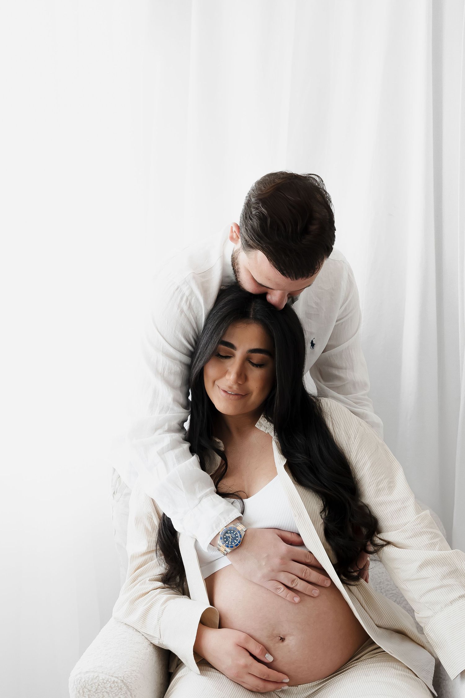 Intimate maternity portraits in white against bright backdrop showing tender moments.