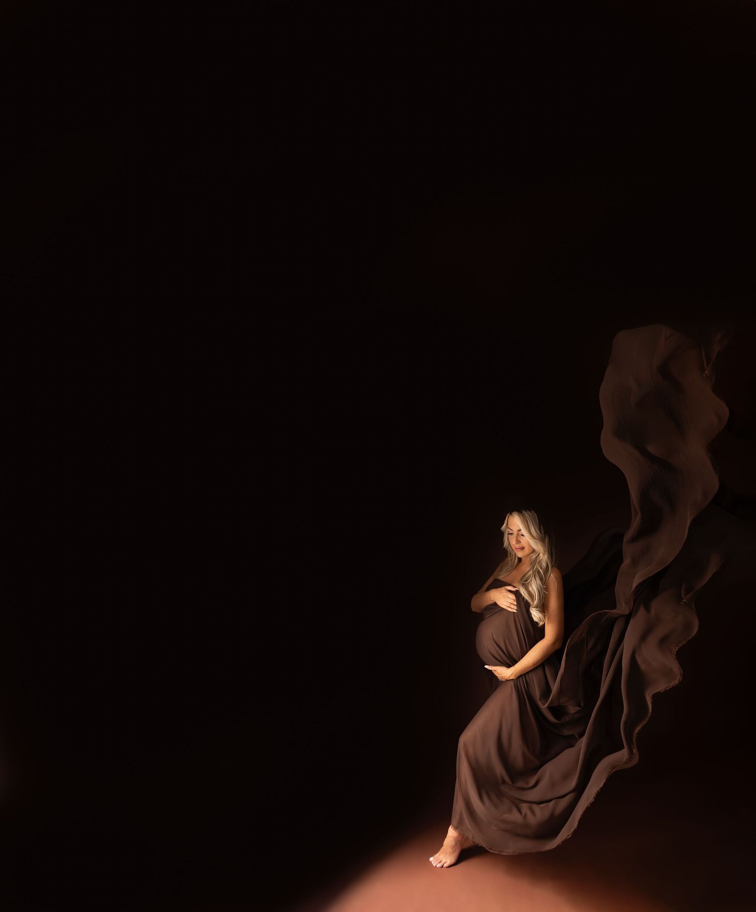 Ethereal maternity photos with flowing fabric against dark backdrop creating dramatic contrast.