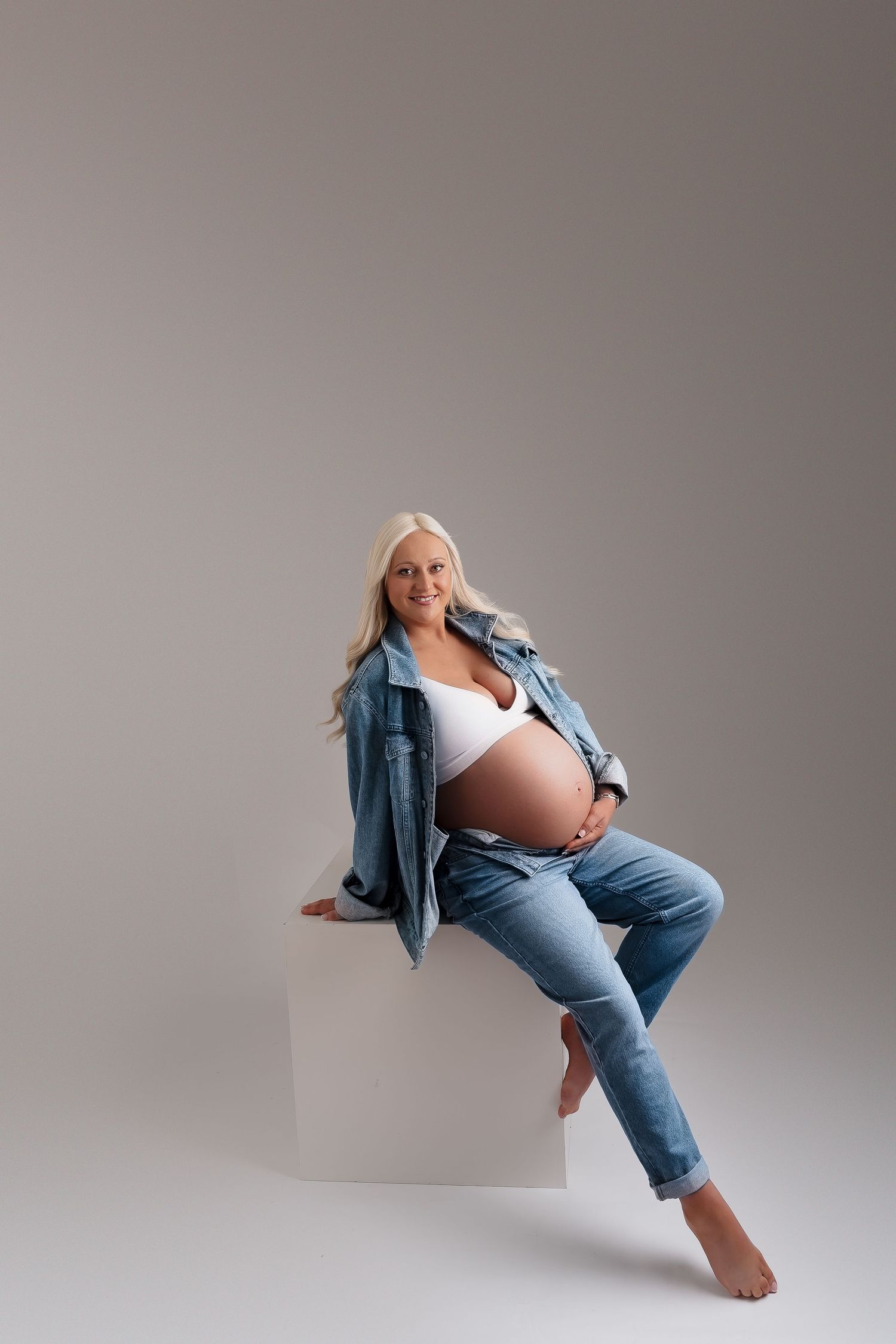 Artistic maternity photoshoot featuring casual denim and neutral backdrop in multiple poses.