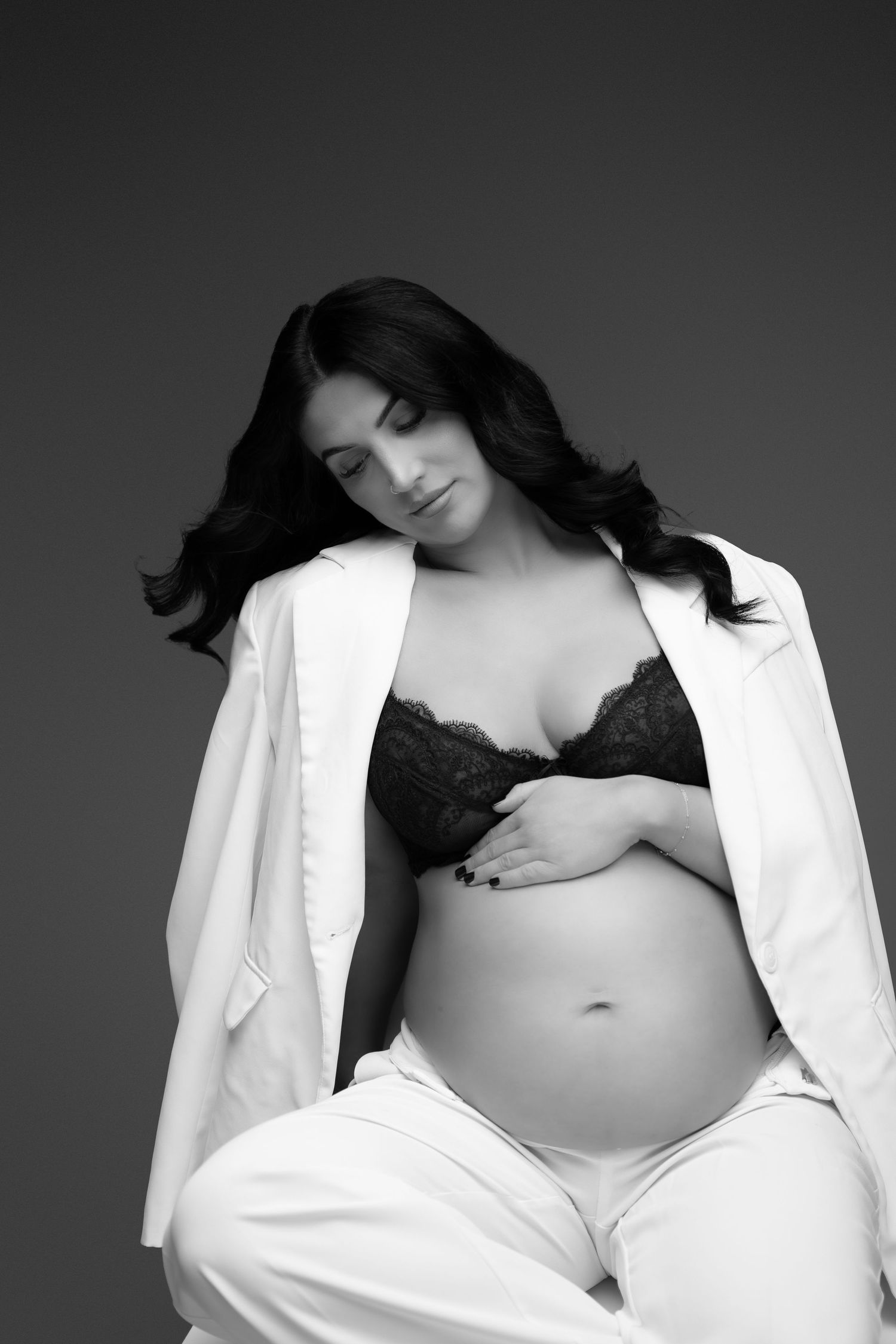 Artistic black and white maternity photo with woman in white open jacket.