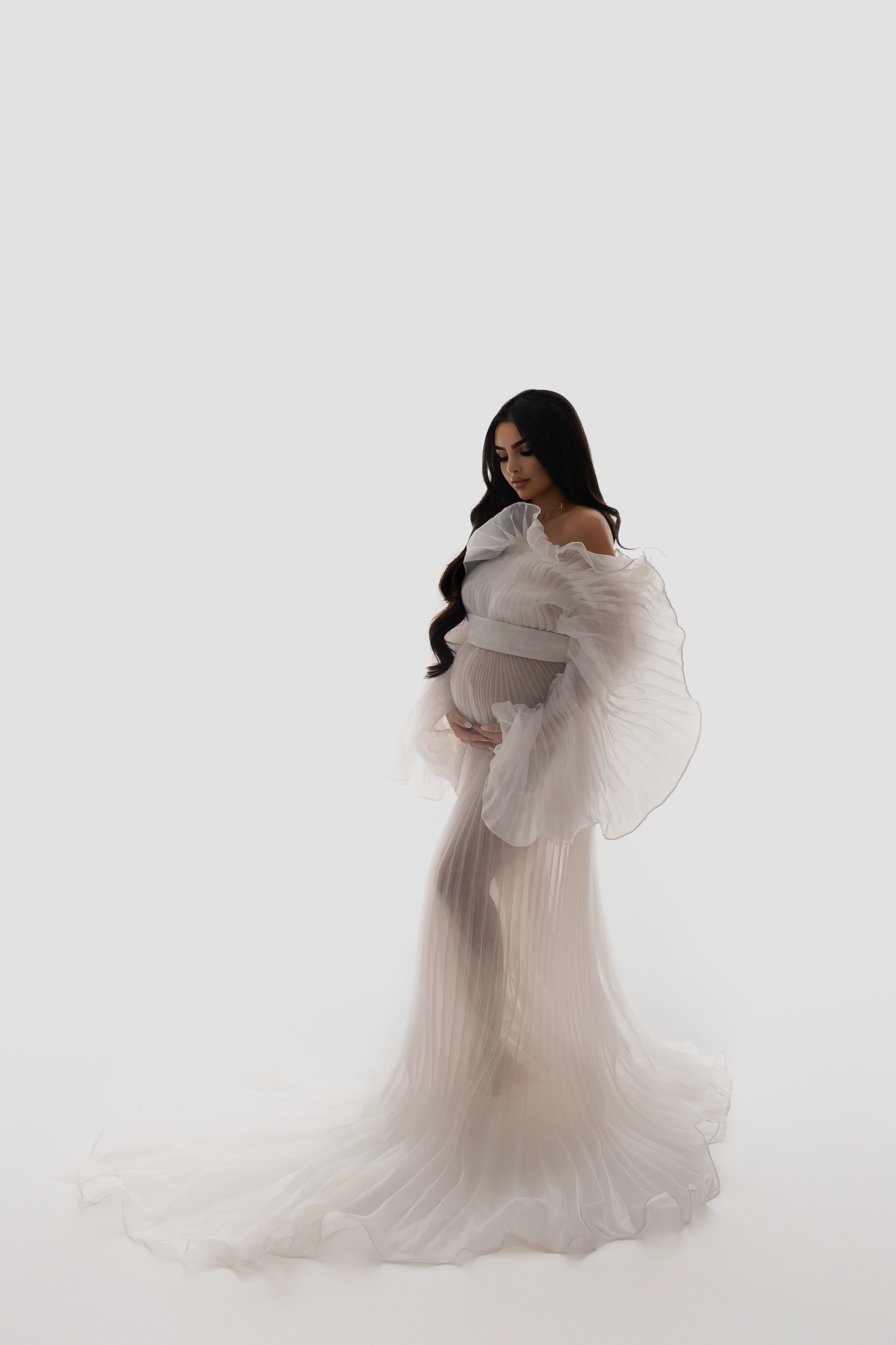 Elegant maternity portrait featuring flowing white dress against light background.