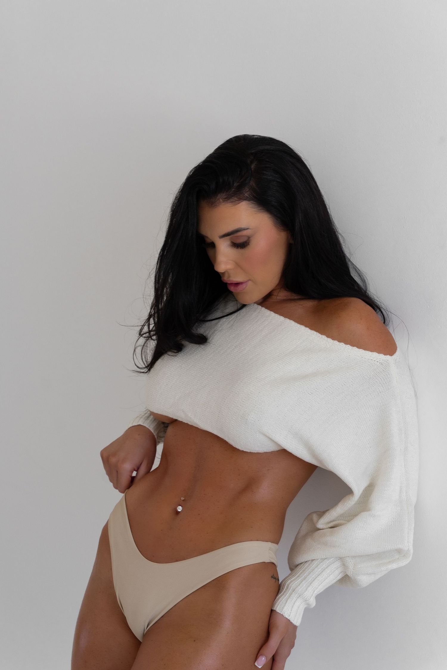 Woman in white crop top poses artistically against minimalist white background.