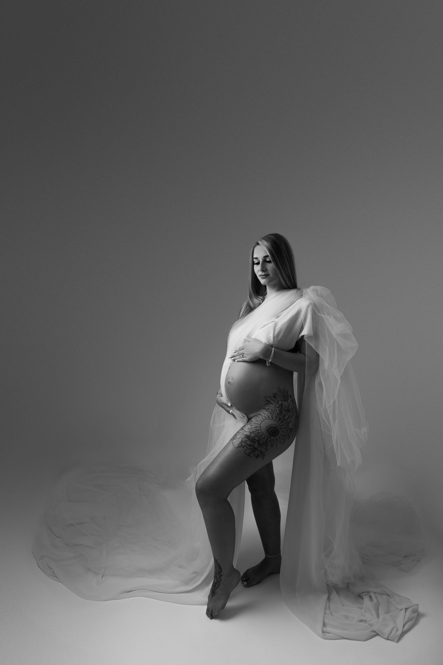 Dramatic black and white maternity portrait with flowing sheer fabric against dark background.