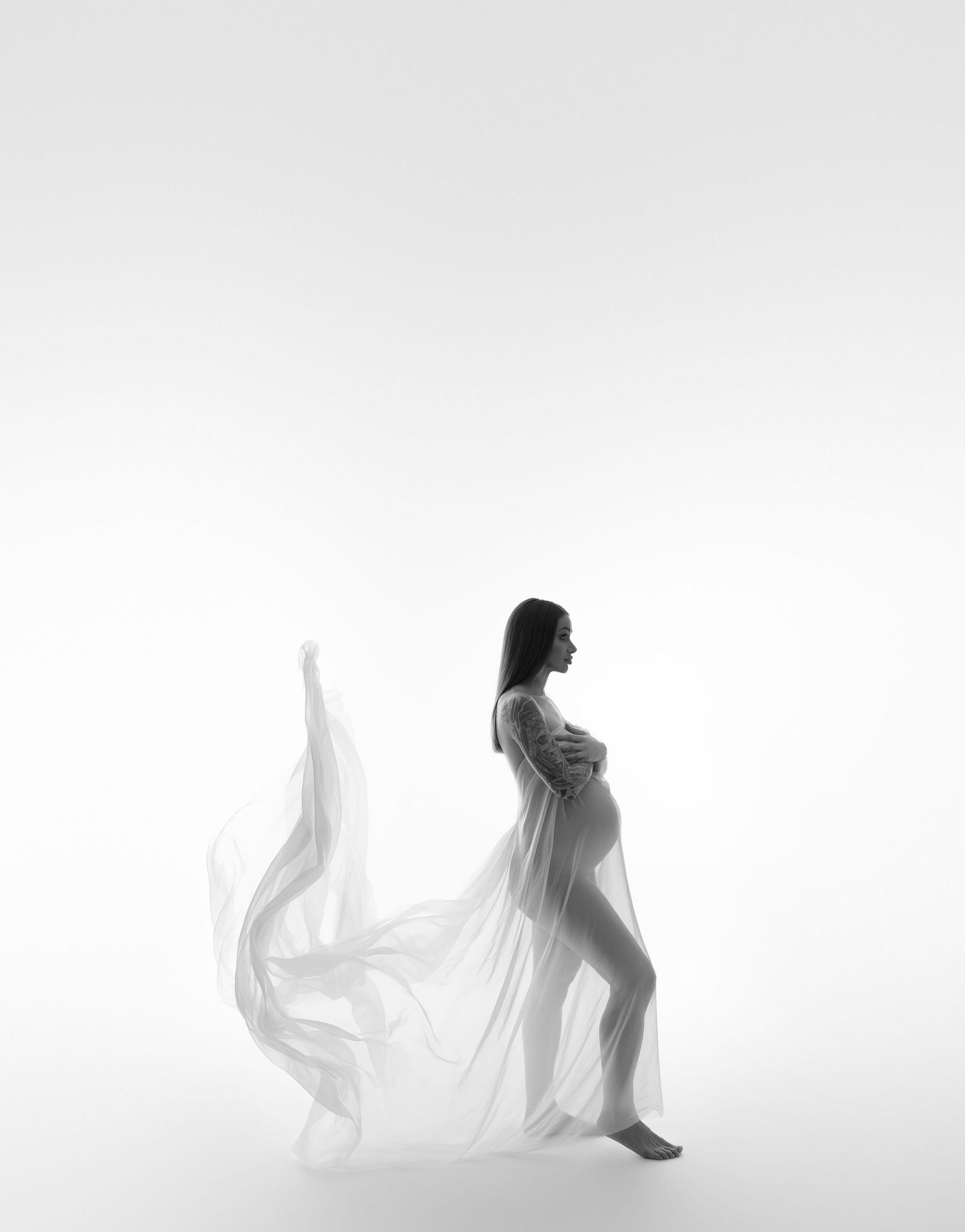 Ethereal black and white maternity photo with flowing white fabric creating movement.